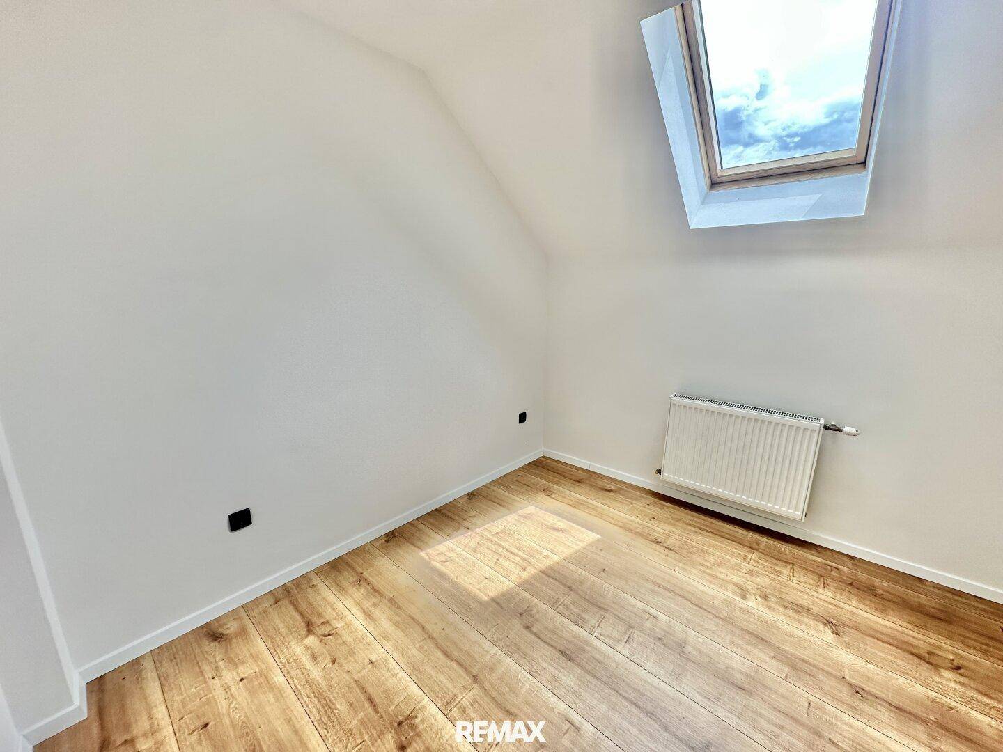 Helles Schlafzimmer im Dachgeschoss mit Holzboden, Dachfenster und Heizkörper.