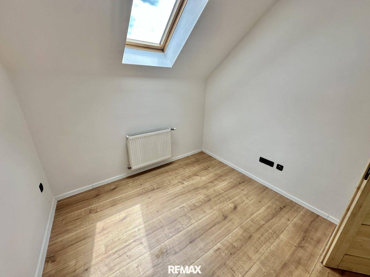Dachgeschoss-Schlafzimmer mit schrägen Wänden, Holzboden und einem großen Dachfenster.