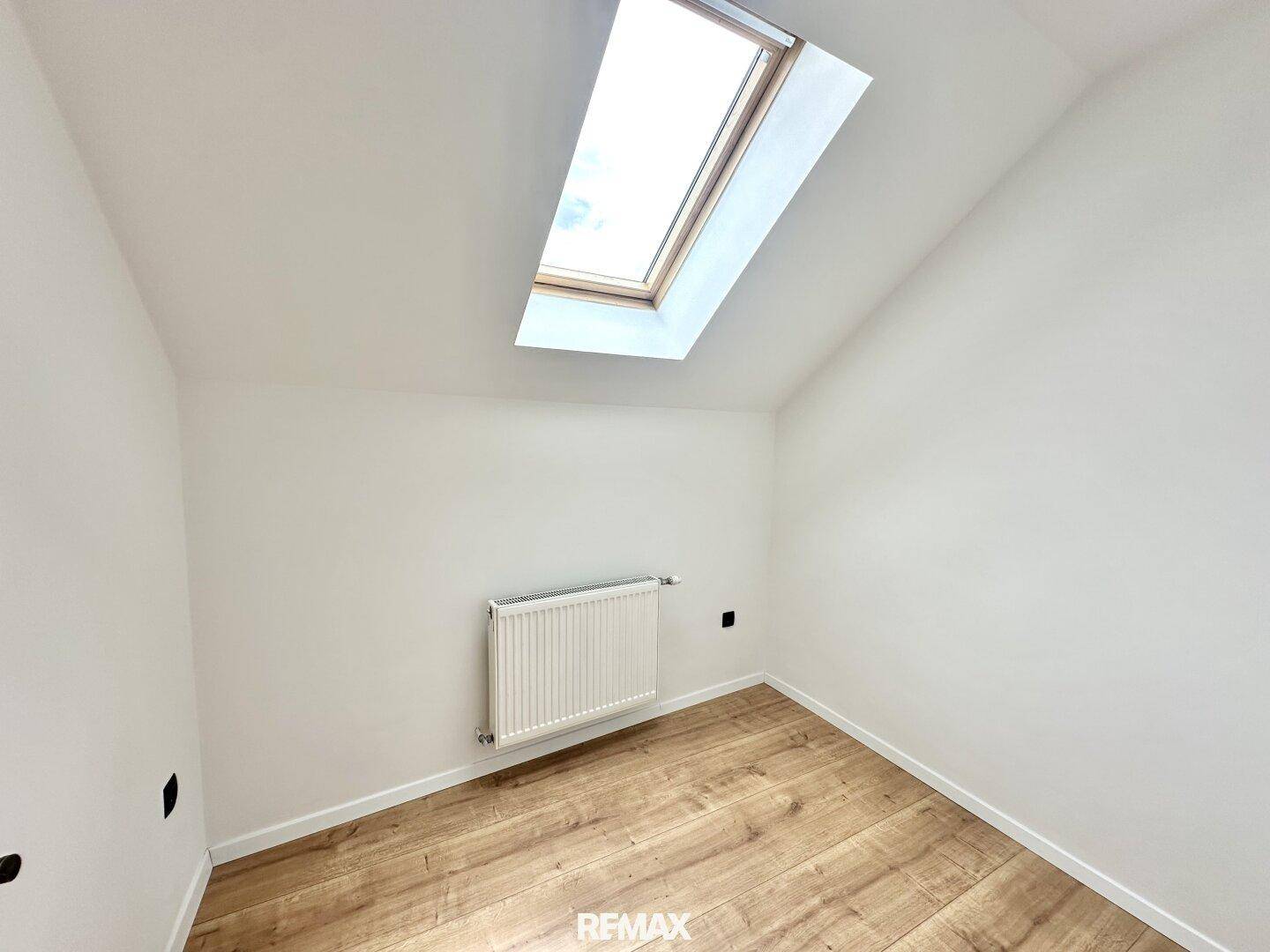 Geräumiges Schlafzimmer mit Holzboden, weiß gestrichenen Wänden und Dachfenster.