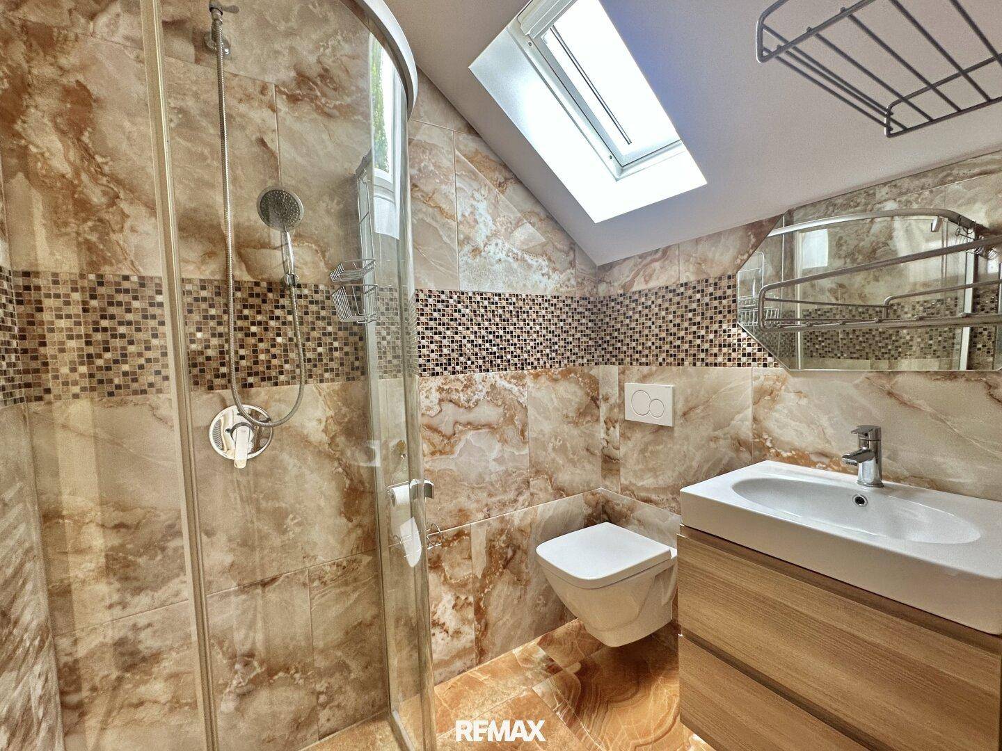 Modernes Badezimmer mit Duschkabine, Wand-WC, Waschtisch und Dachfenster.