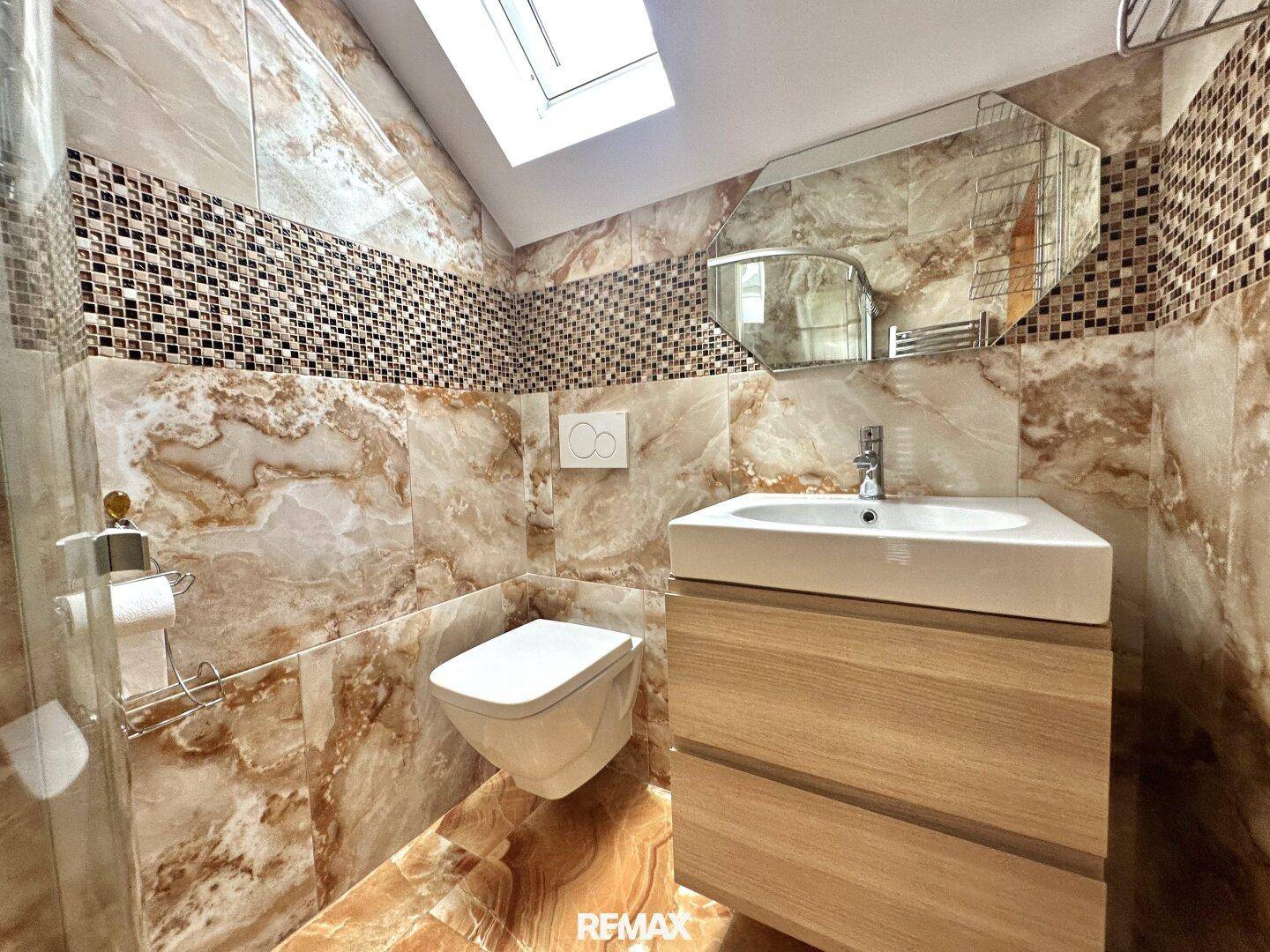 Helles Badezimmer mit Waschtisch, Wand-WC, gefliesten Wänden und Dachfenster.