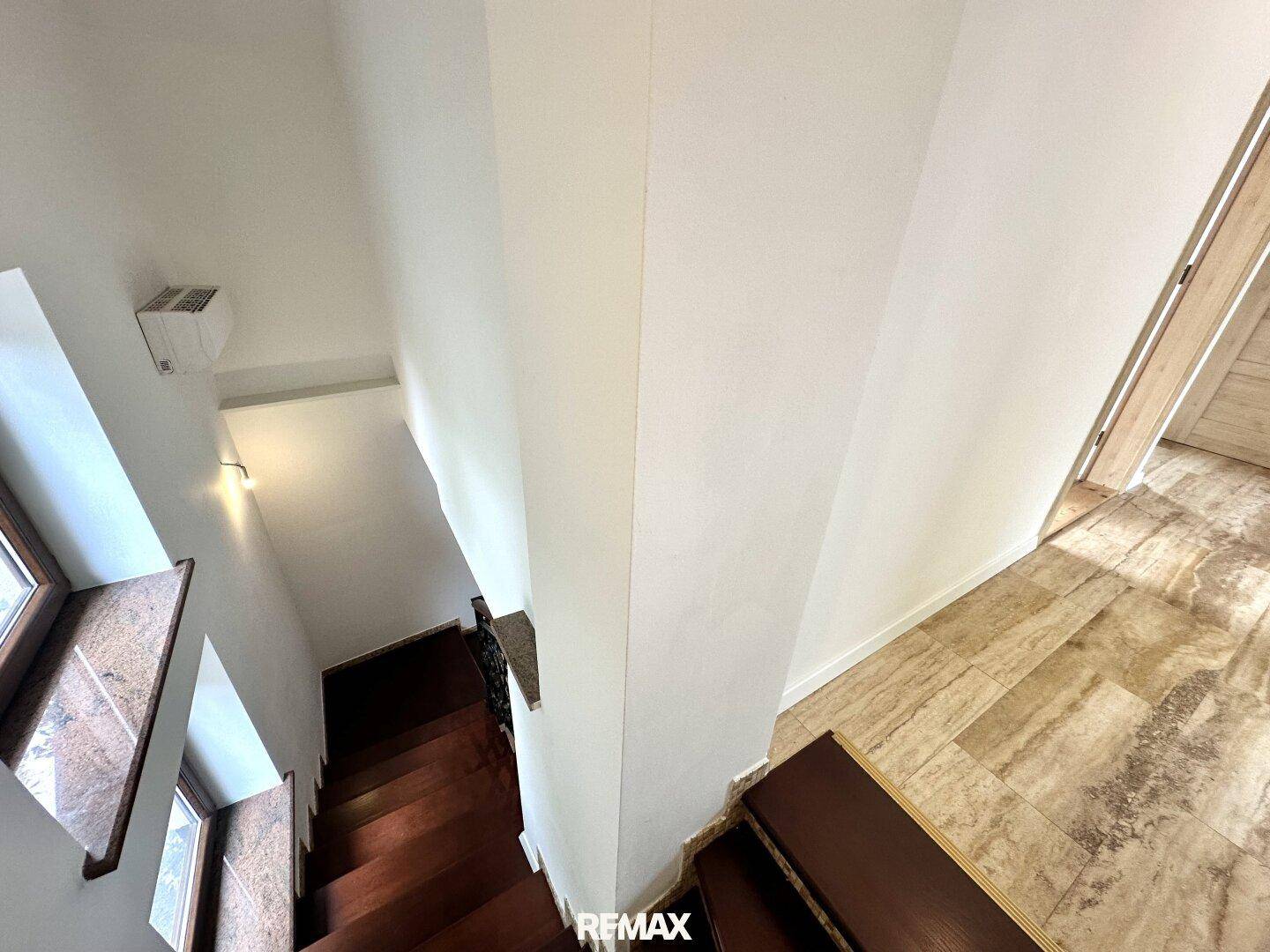 Treppenhaus mit Holzstufen und weiß gestrichenen Wänden, die nach unten führen.
