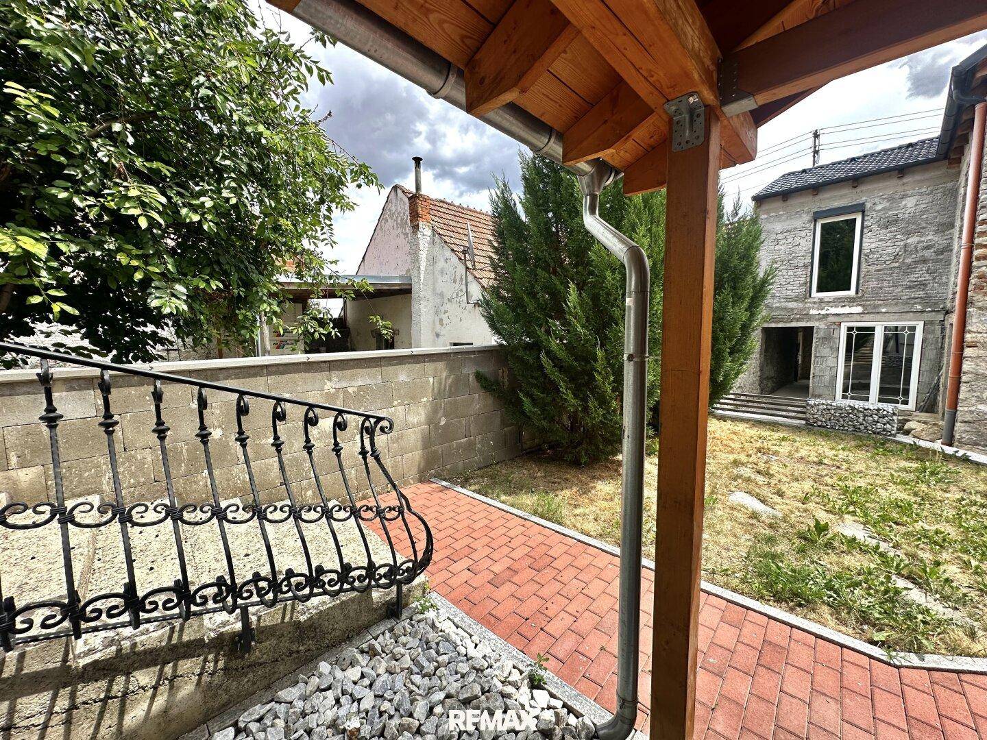 Seitenansicht des Grundstücks mit altem Gebäude und neuem überdachtem Bereich.