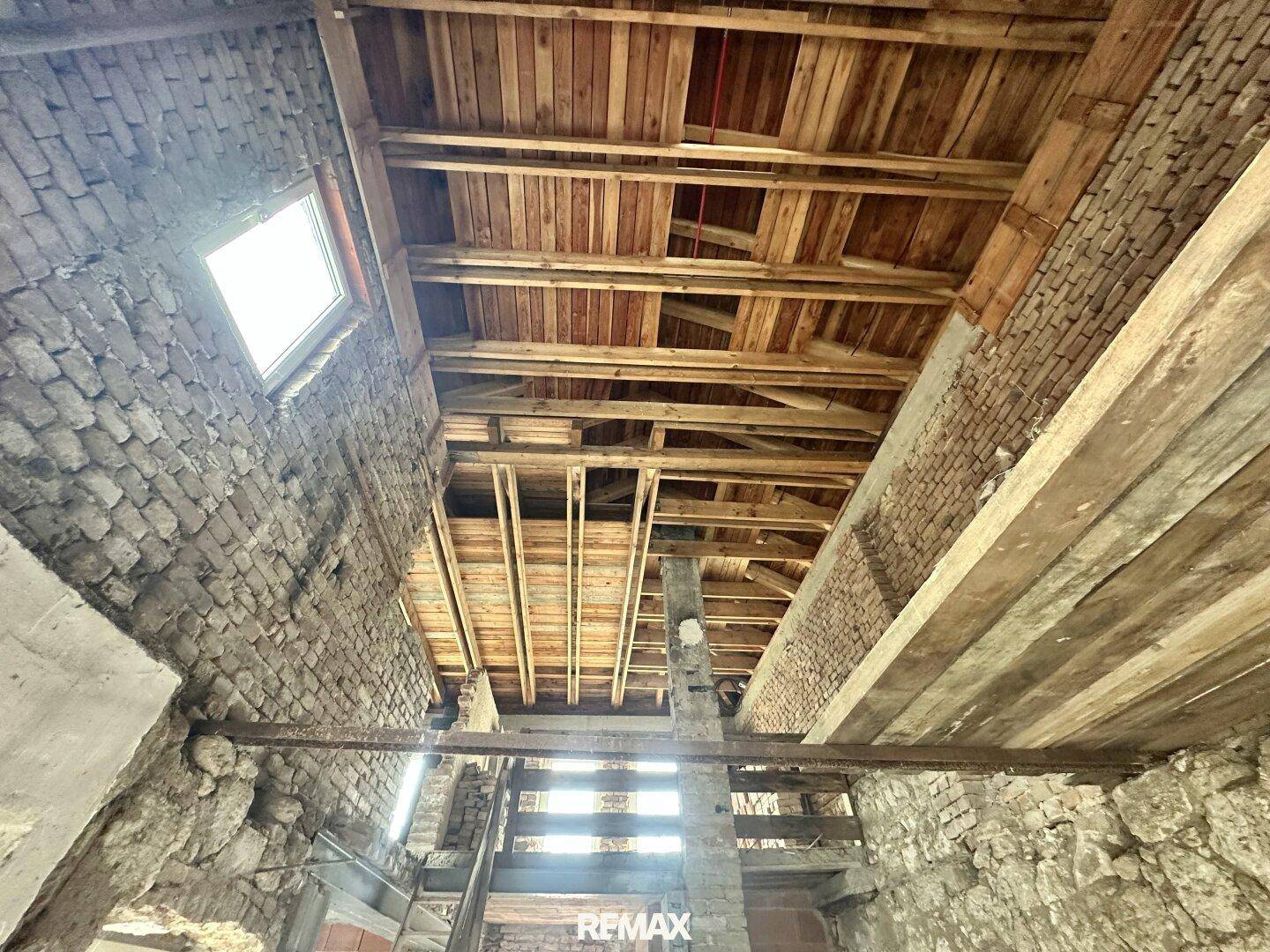 Unausgebauter Dachboden des alten Gebäudes mit sichtbaren Holzbalken und Ziegelwänden.