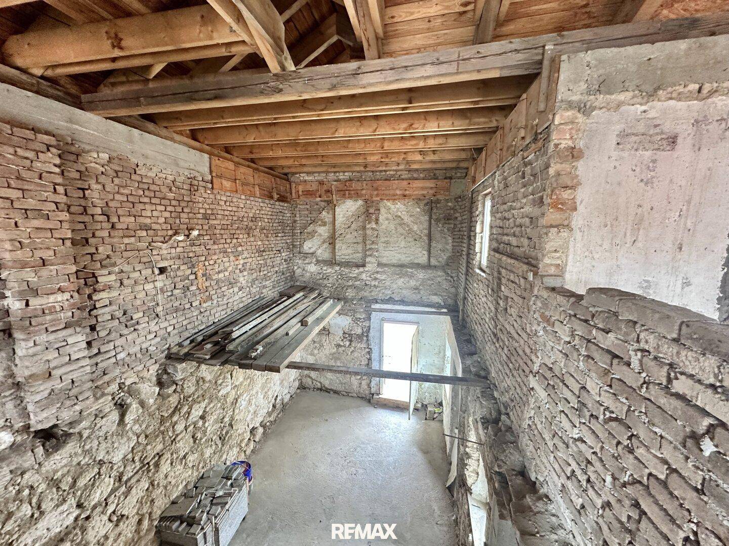 Geräumiges Dachgeschoss im Rohbau mit sichtbaren Holzbalken und Ziegelwänden.
