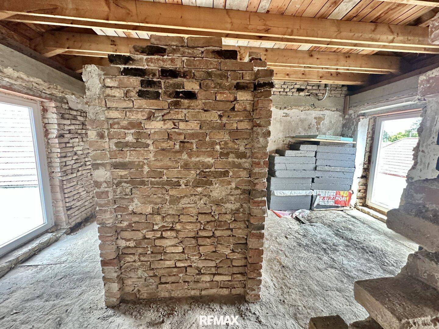 Dachgeschoss im Rohbau mit zentralem Ziegelkamin, Holzdachstuhl und Fenstern.
