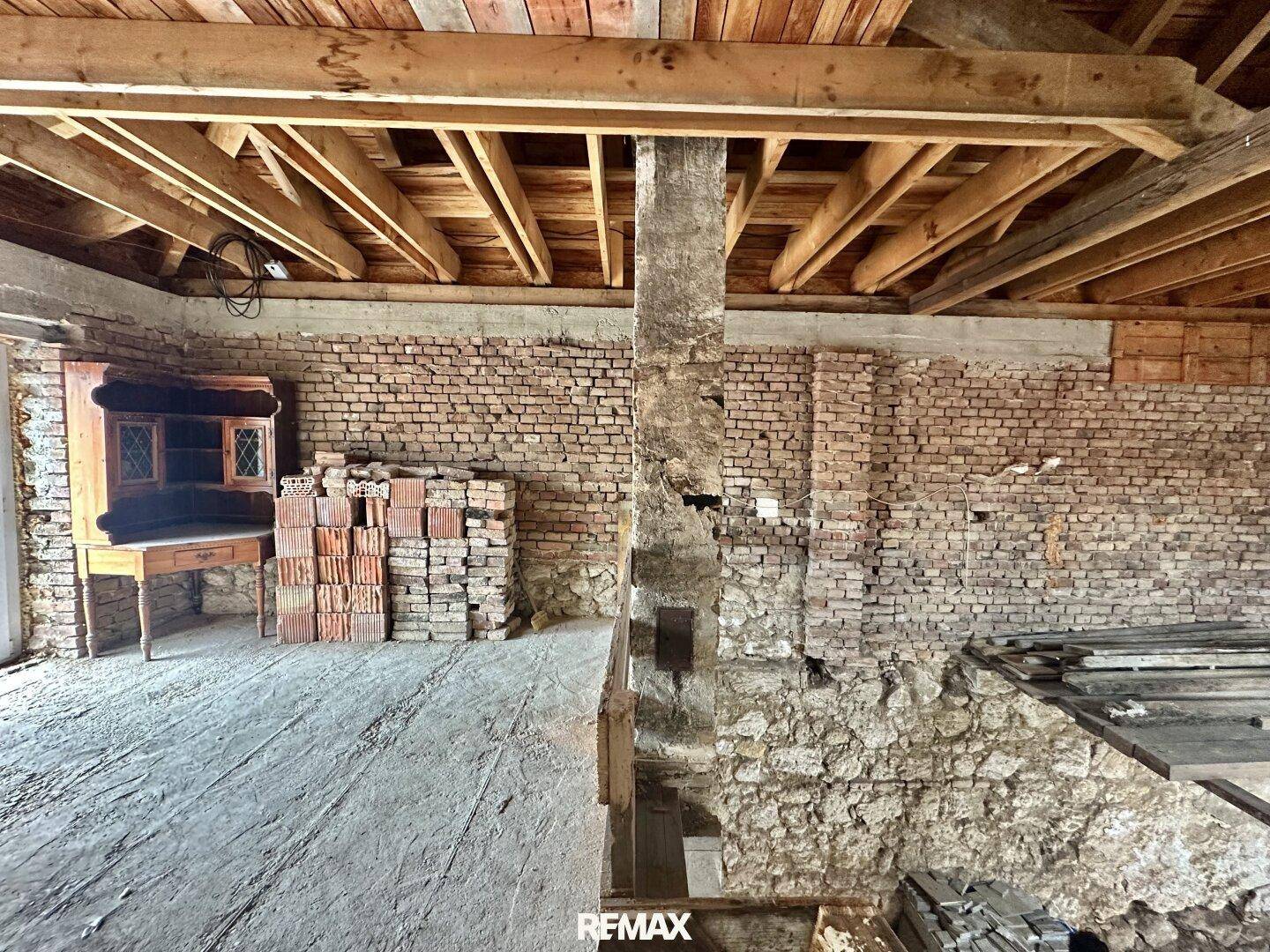 Geräumiges Dachgeschoss im Rohbau mit Holzdachstuhl und freiliegenden Ziegelwänden.