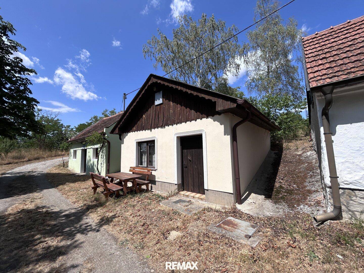 Ländliches Haus mit einfacher Fassade und Holztisch im Freien an einem sonnigen Tag.