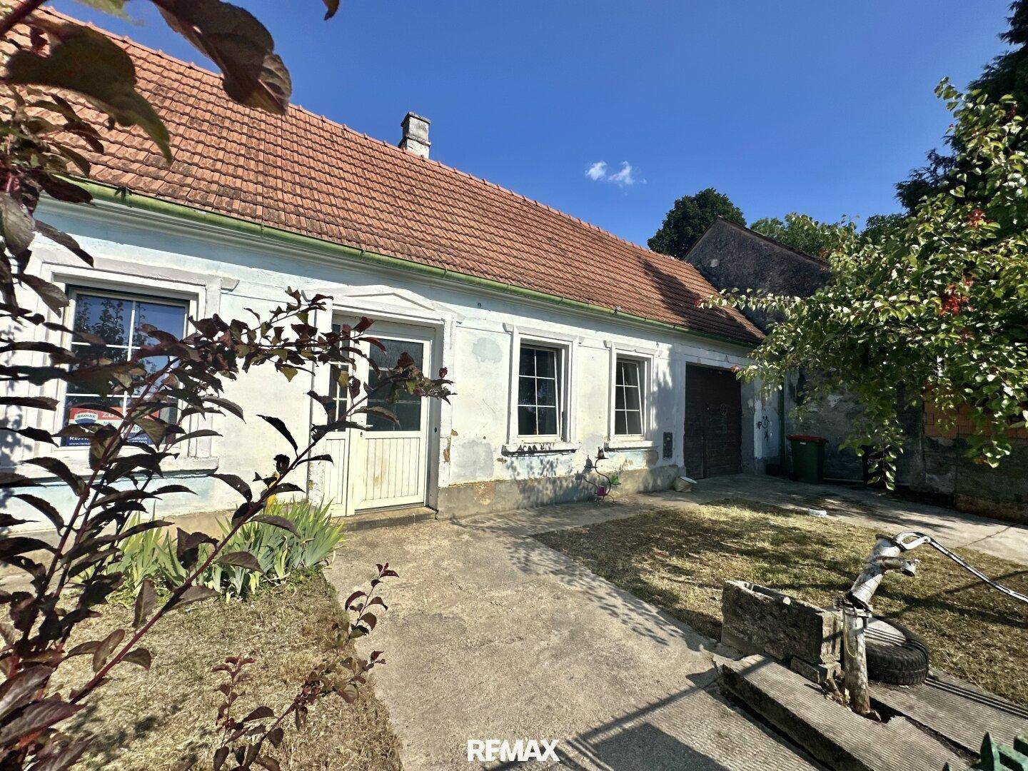 Ansicht des alten Hauses von vorne mit Garten, Bäumen und einem gepflasterten Zugangsweg.