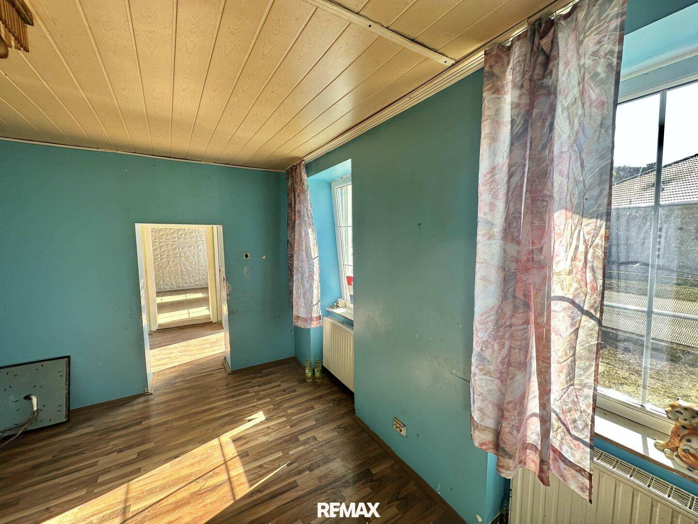 Geräumiges Zimmer mit blauen Wänden, Holzdecke und Holzboden, bereit zur Renovierung.