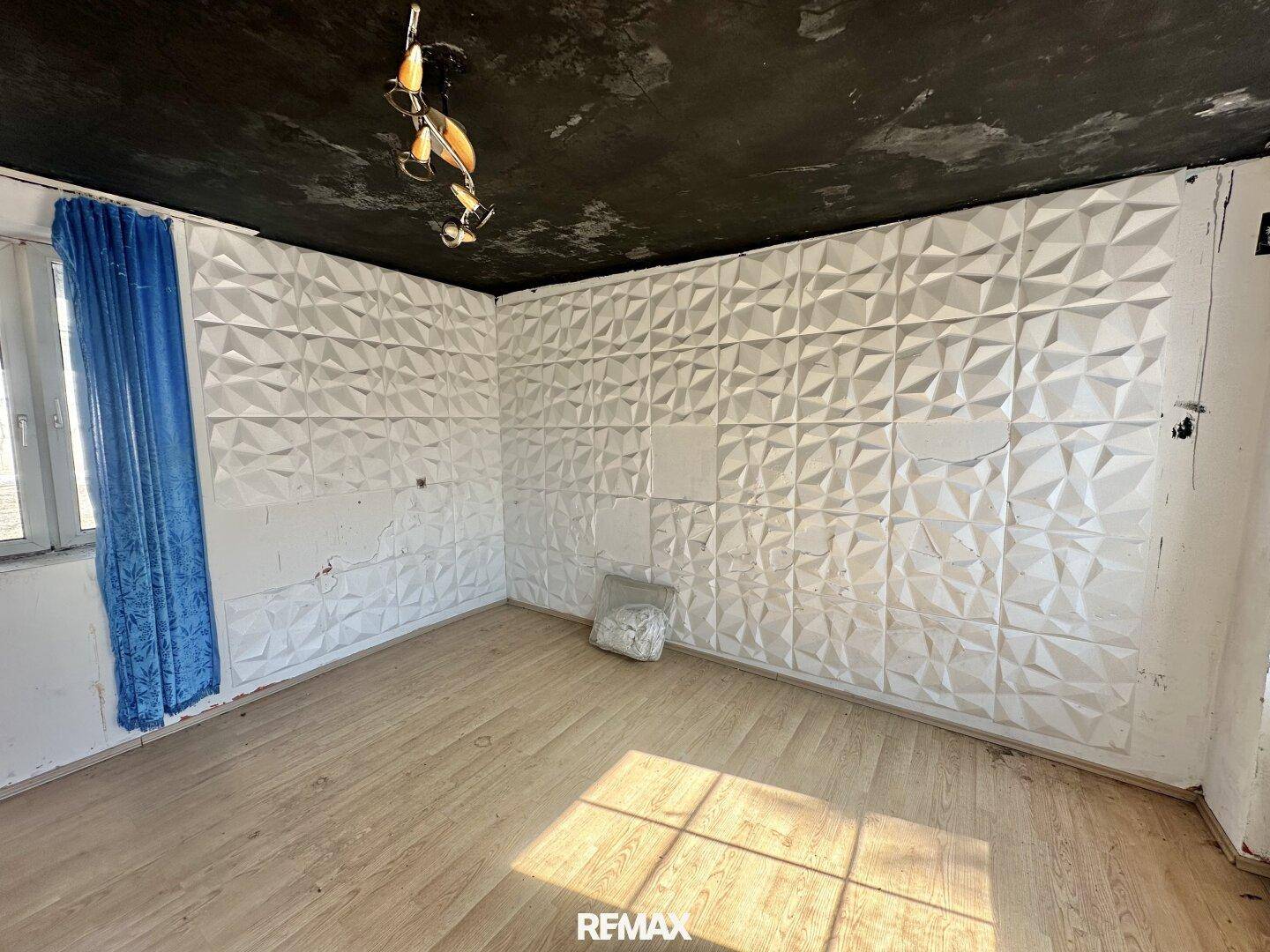 Zimmer mit auffälliger 3D-Wandverkleidung, dunkler Decke und Holzboden.