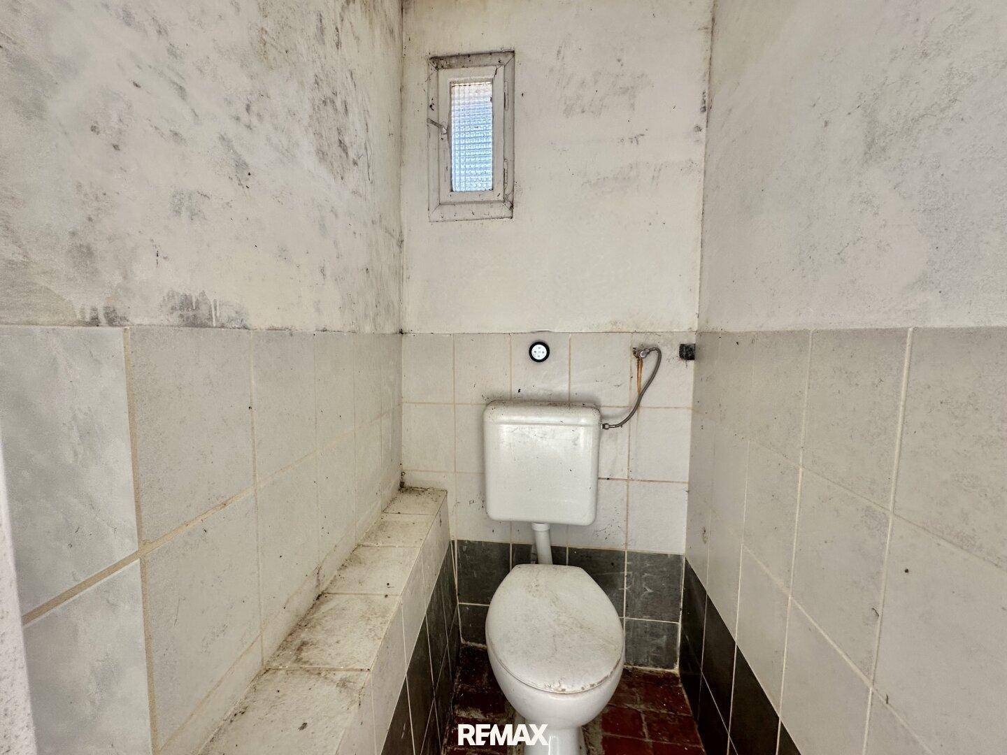 Einfache Toilette mit Fliesen an den Wänden und einem kleinen Fenster.