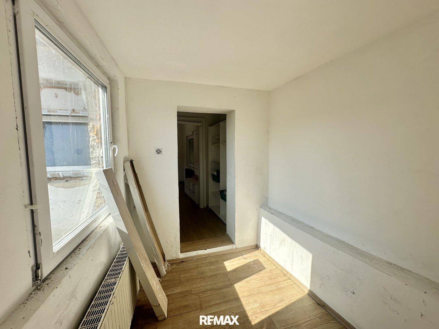 Heller, leerer Raum mit Fenster, Heizkörper und Holzboden, der auf Renovierung wartet.