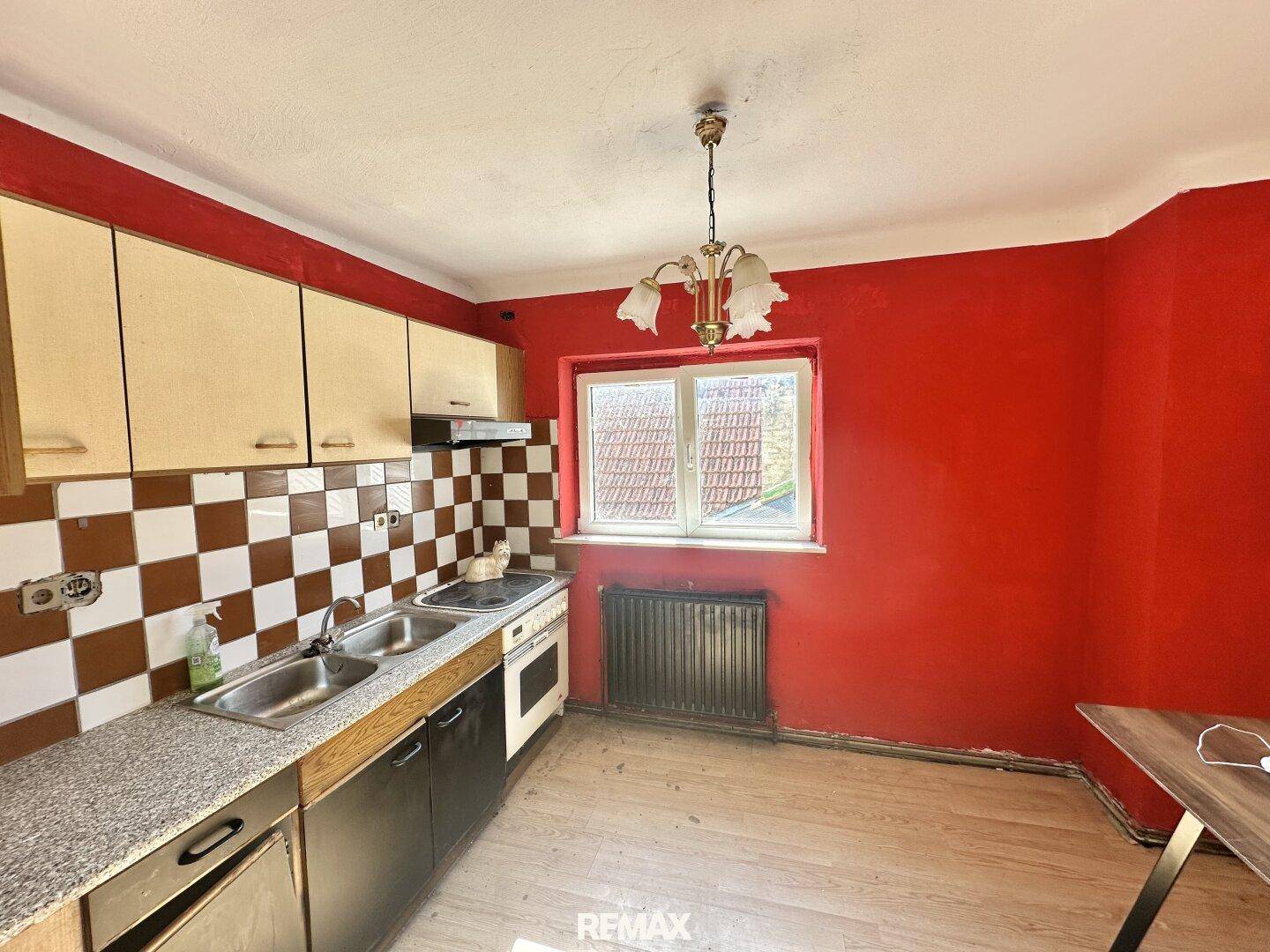 Küche mit roter Wand, karierten Fliesen, Spüle und einem Fenster mit Blick nach draußen.