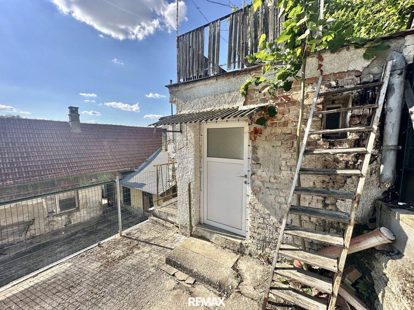 Alter Außenbereich mit einer Betonfläche, einer Tür und einer provisorischen Holztreppe.