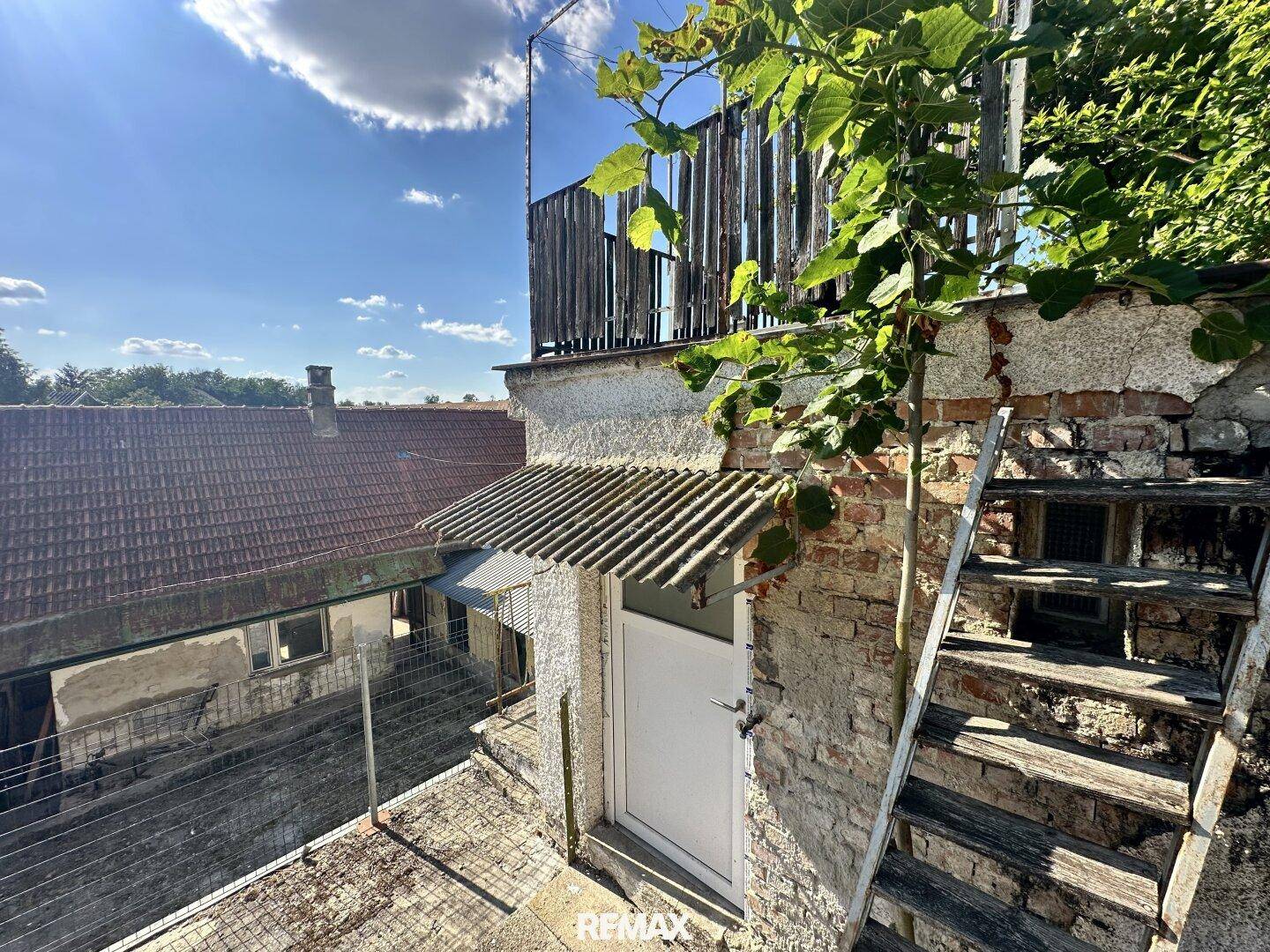 Alte Terrasse mit einer Tür, einer Holztreppe und Blick auf die Nachbargebäude.