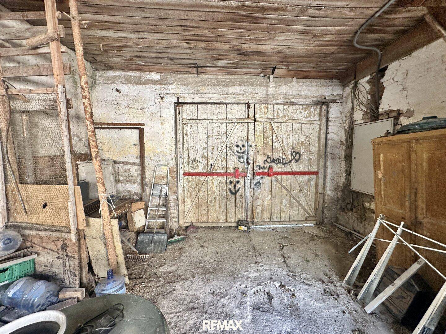 Geräumige Garage oder Lagerraum mit Holztüren, sichtbaren Holzbalken und viel Unordnung.