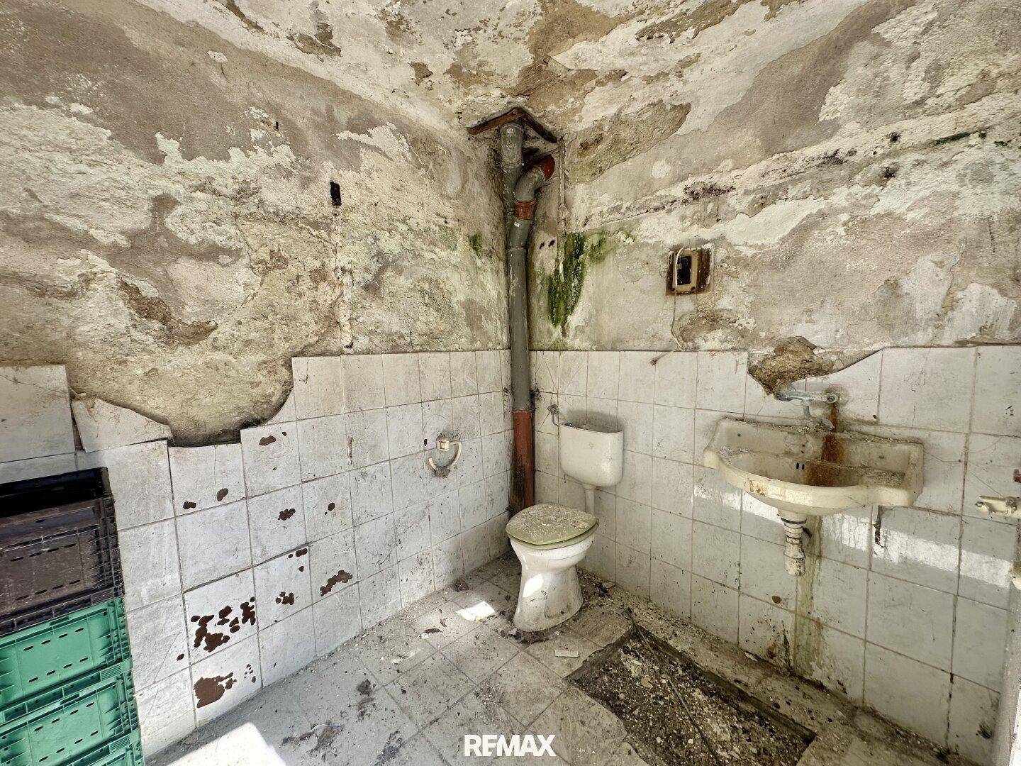 Kleine Toilette mit Waschbecken und Fliesen in sehr schlechtem, stark sanierungsbedürftigem Zustand.