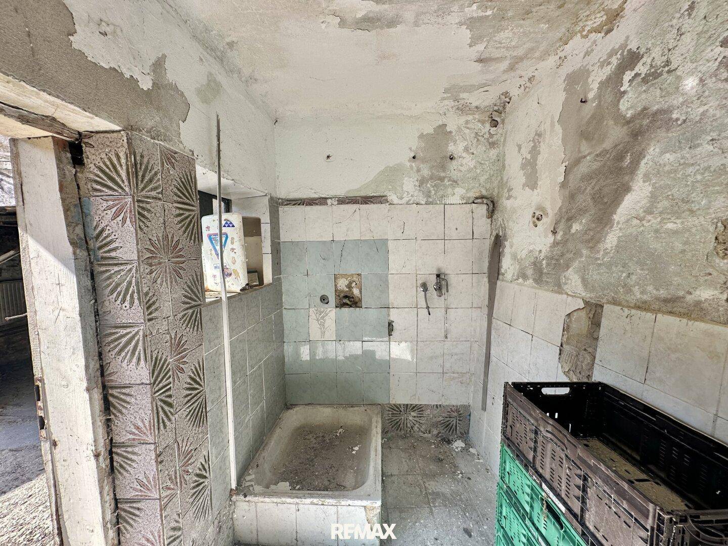 Badezimmer mit kleiner Badewanne und alten Fliesen, stark sanierungsbedürftig und unaufgeräumt.