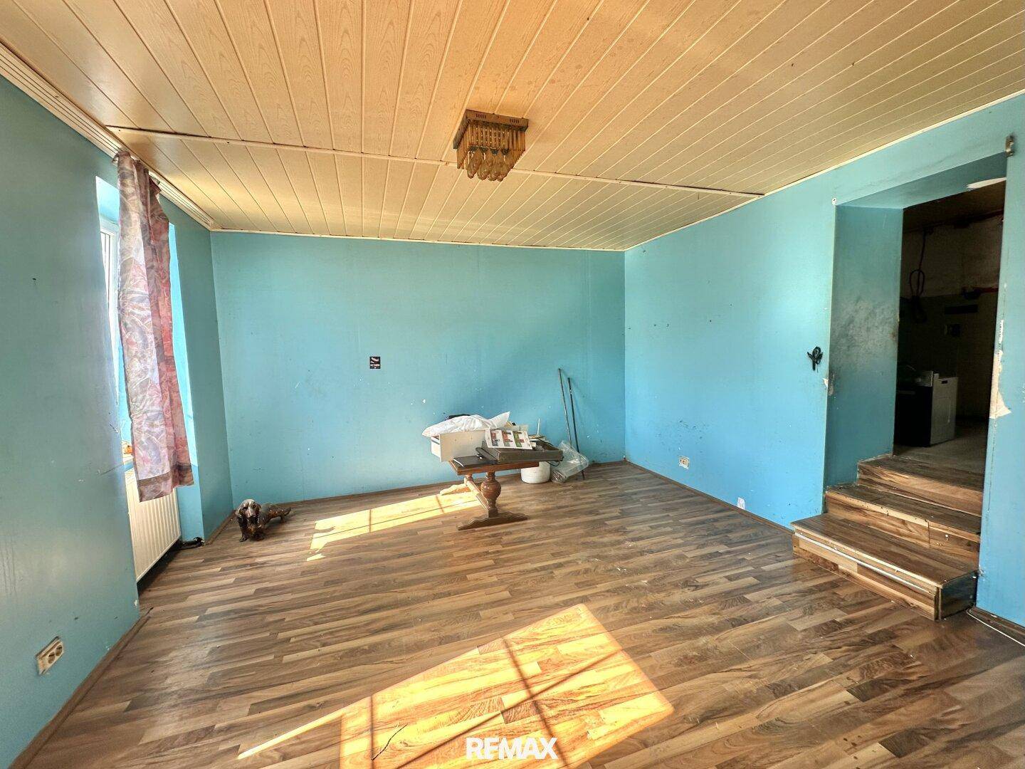 Helles Wohnzimmer mit blauen Wänden, Holzdecke und Holzboden, mit Treppenaufgang.