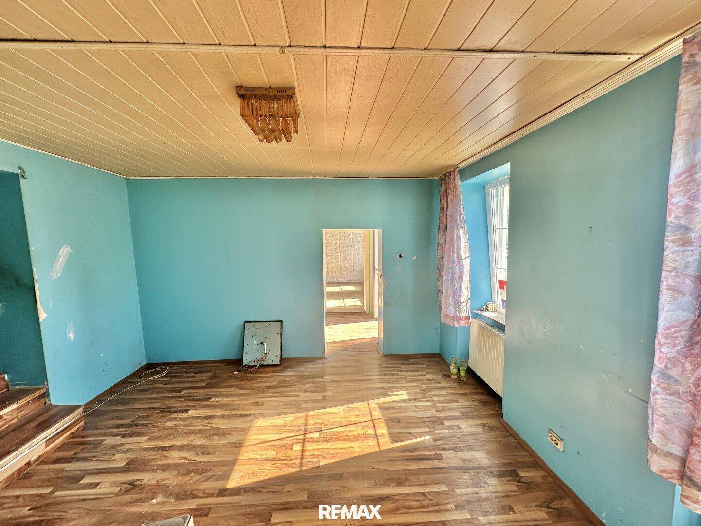 Geräumiges Zimmer mit blauen Wänden, Holzdecke und Holzboden, mit Blick in den nächsten Raum.