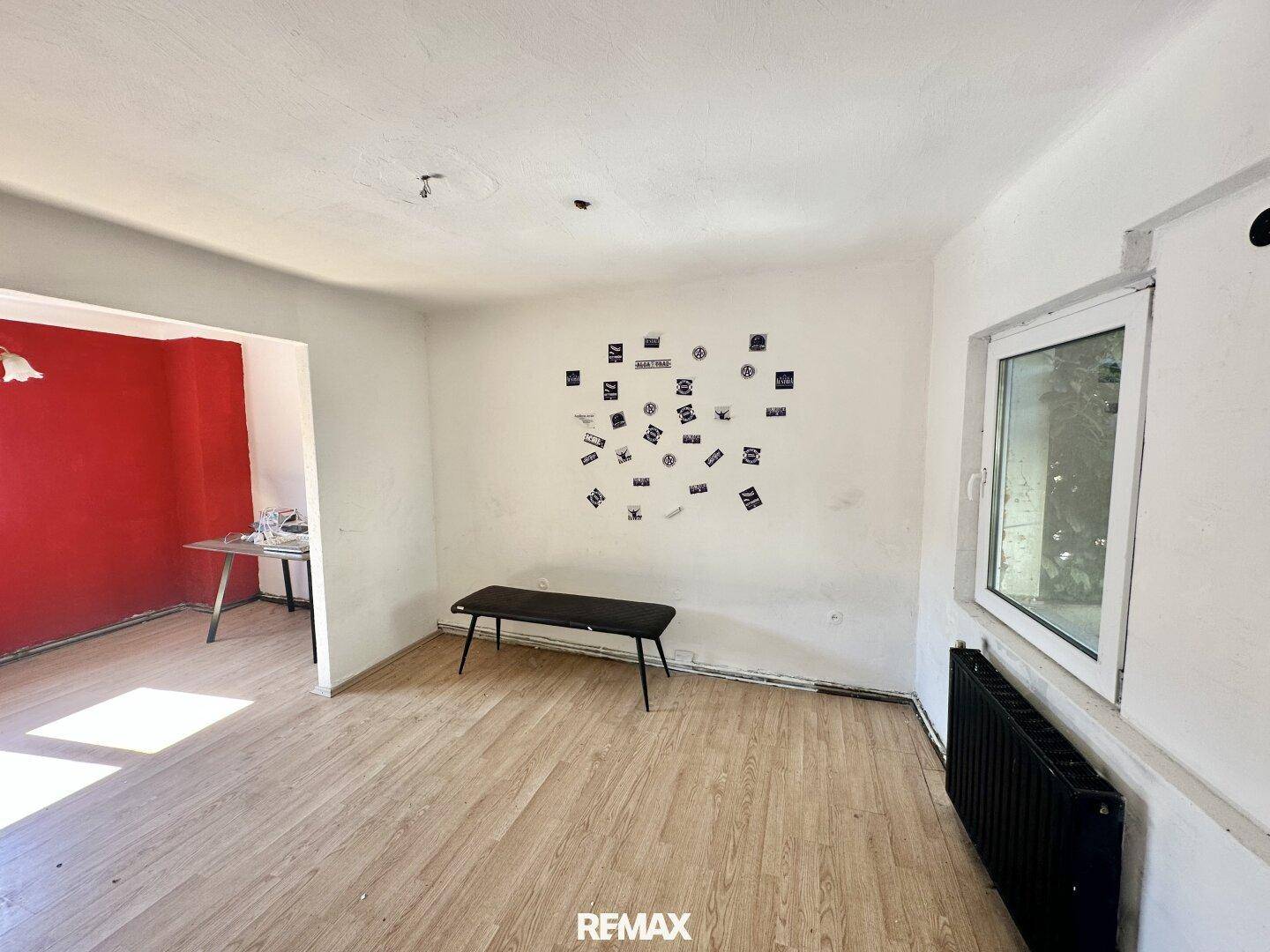 Geräumiges Wohnzimmer mit Holzboden, weiß gestrichenen Wänden und einem Fenster.