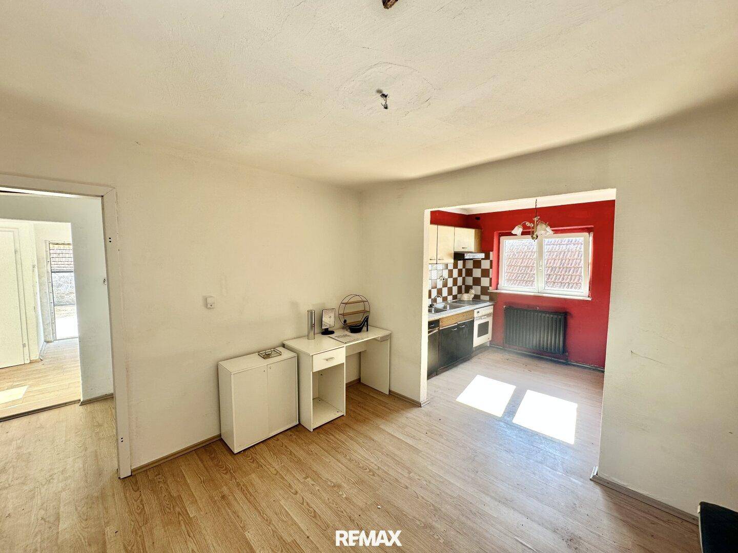 Offener Wohnbereich mit Holzboden, der in eine Küche mit roter Wand übergeht.