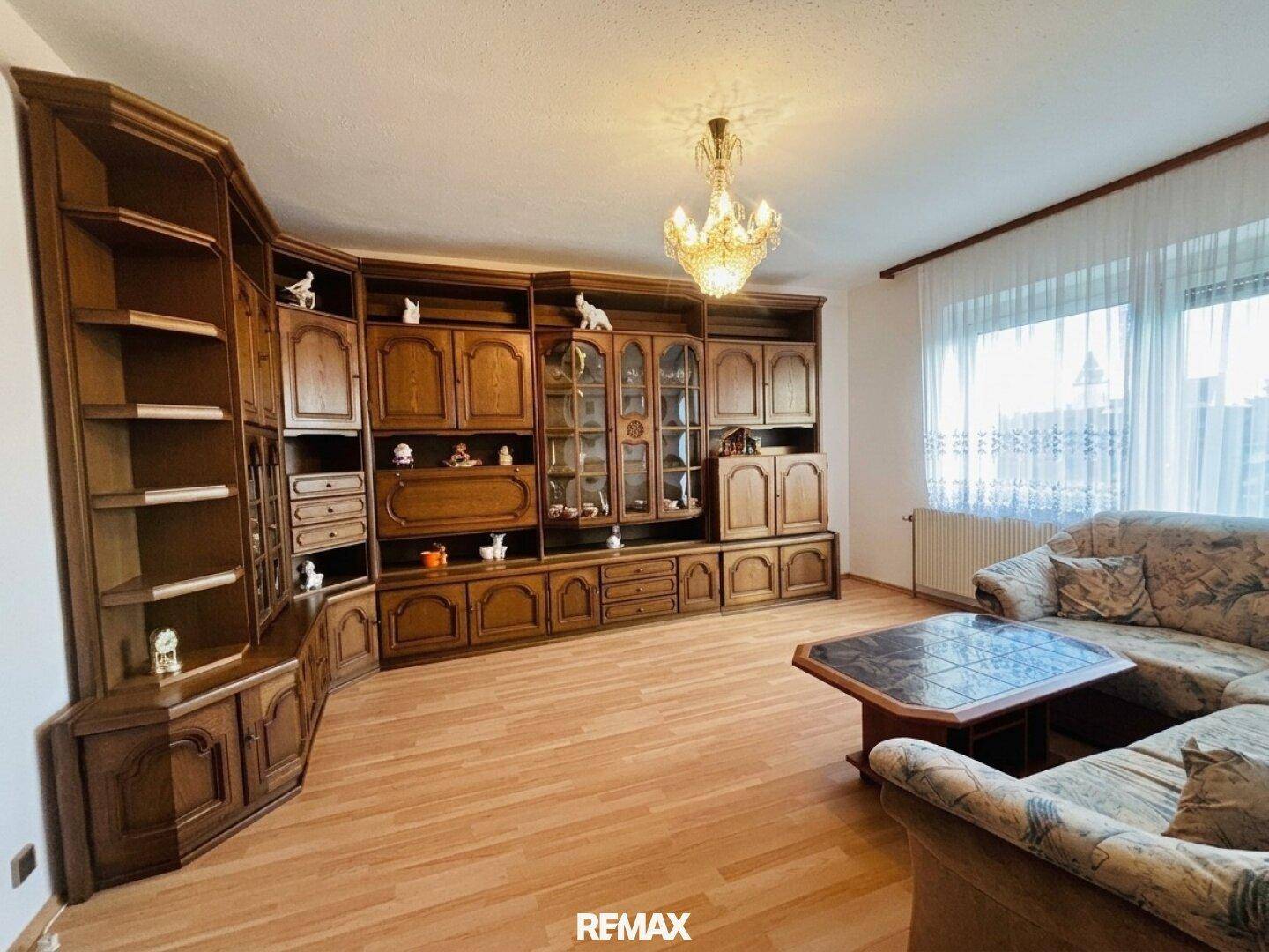 Geräumiges Wohnzimmer mit großer Holzschrankwand, bequemer Couch und Kronleuchter.