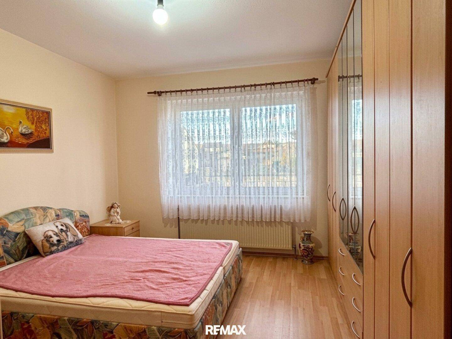 Schlafzimmer mit Doppelbett, Holzschrank und großem Fenster für viel Tageslicht.