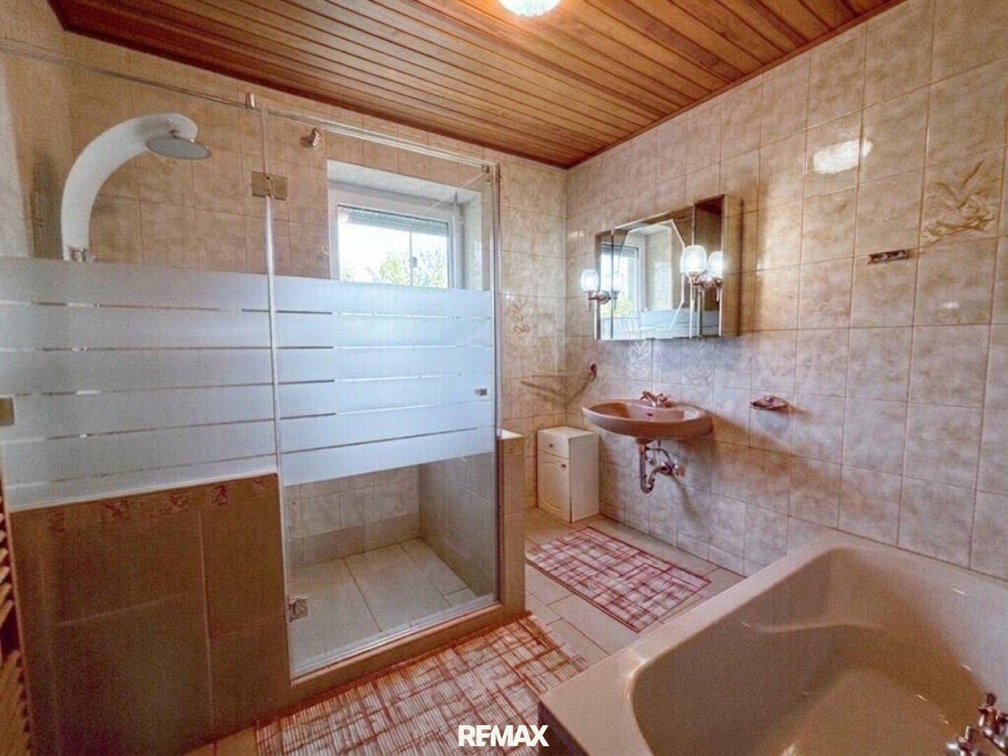 Gefliestes Badezimmer mit Dusche, Badewanne und Holzdecke, ausgestattet mit einem Fenster.