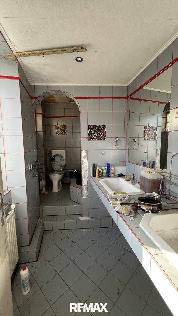 Veraltetes Badezimmer mit grauen Fliesen, roten Akzenten und zwei Waschbecken.
