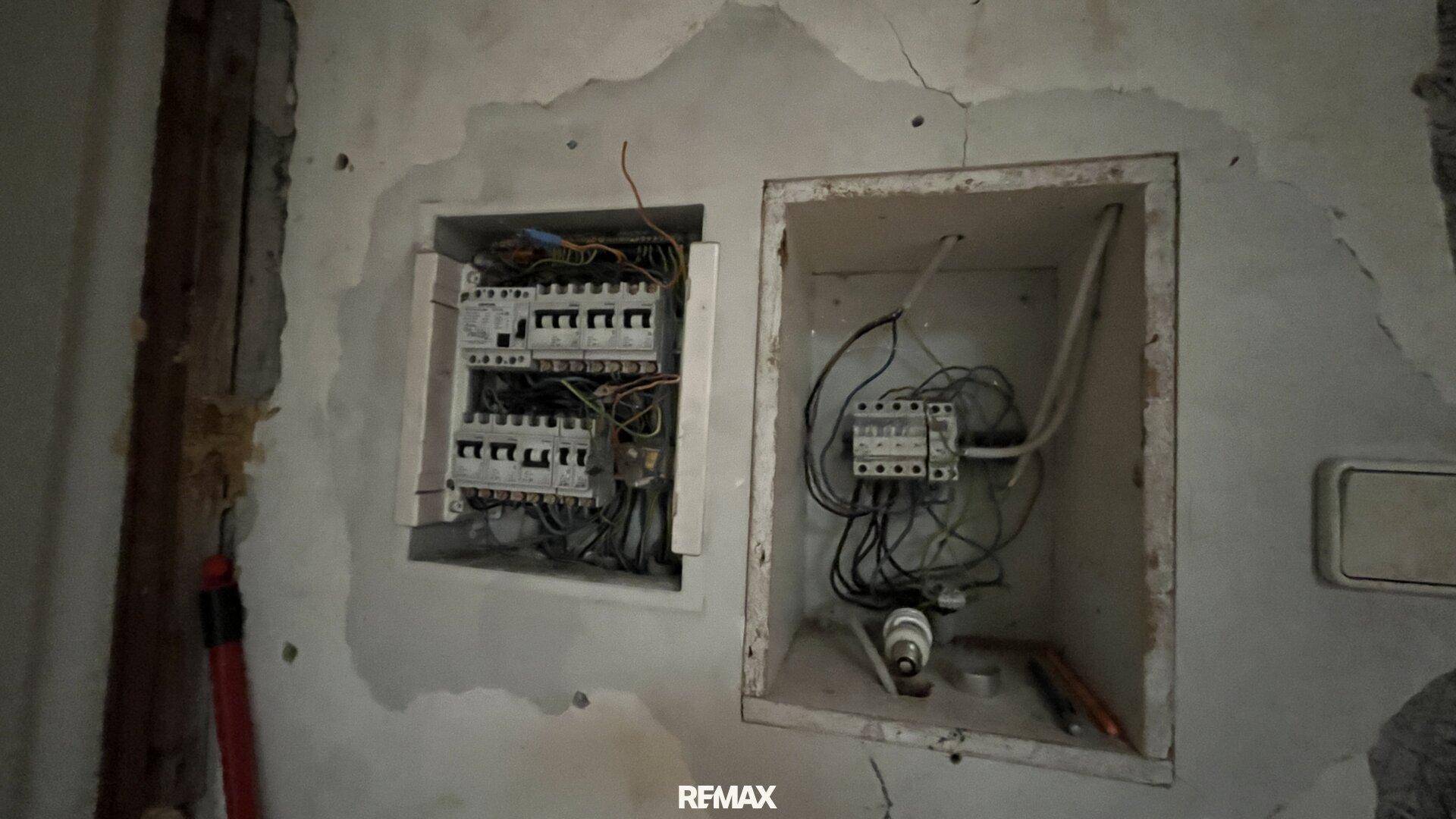 Offener Sicherungskasten mit freiliegenden Kabeln, der den Renovierungsbedarf der Elektrik zeigt.