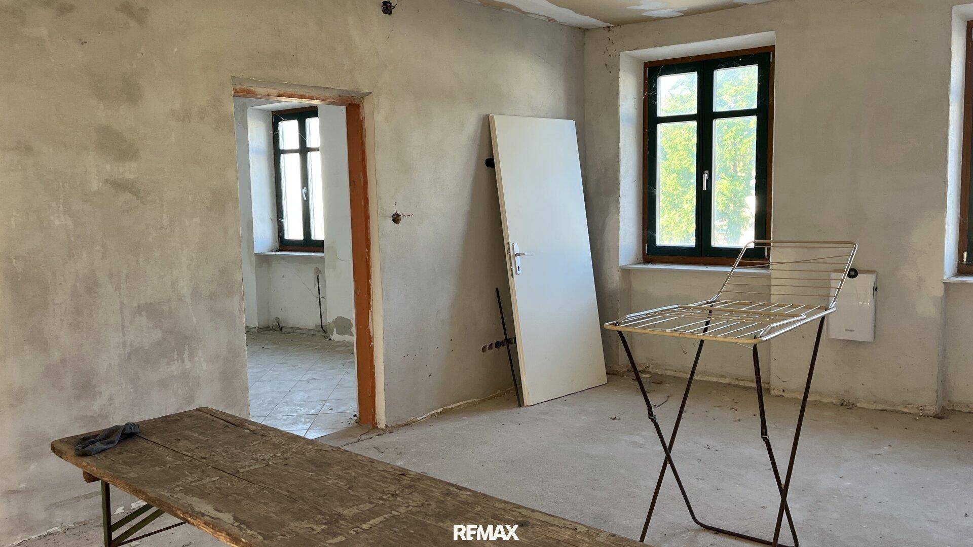 Raum mit Renovierungsbedarf, unverputzten Wänden und einem Fenster mit Blick ins Grüne.