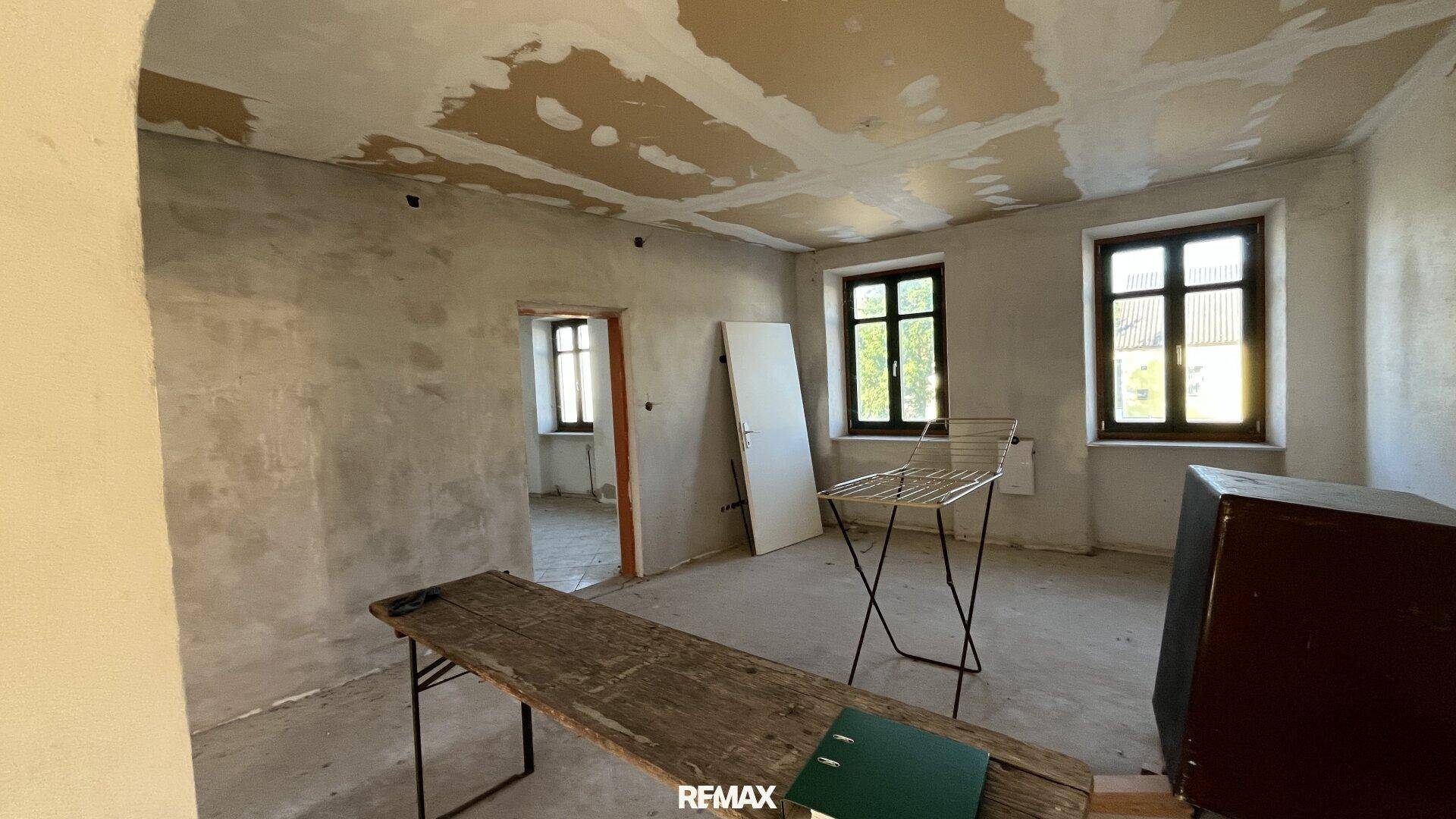 Raum mit Renovierungsbedarf, unverputzten Wänden und einem Fenster mit Blick ins Grüne.