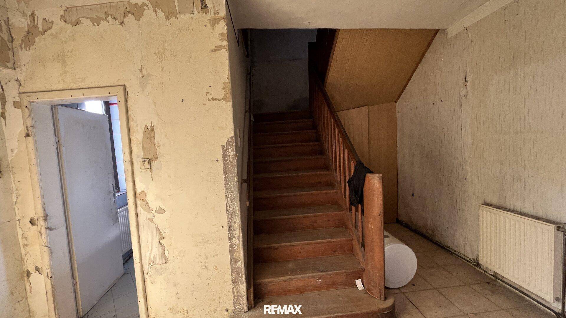 Alter Flur mit Holztreppe und abblätternder Tapete, der Renovierungsbedarf zeigt.