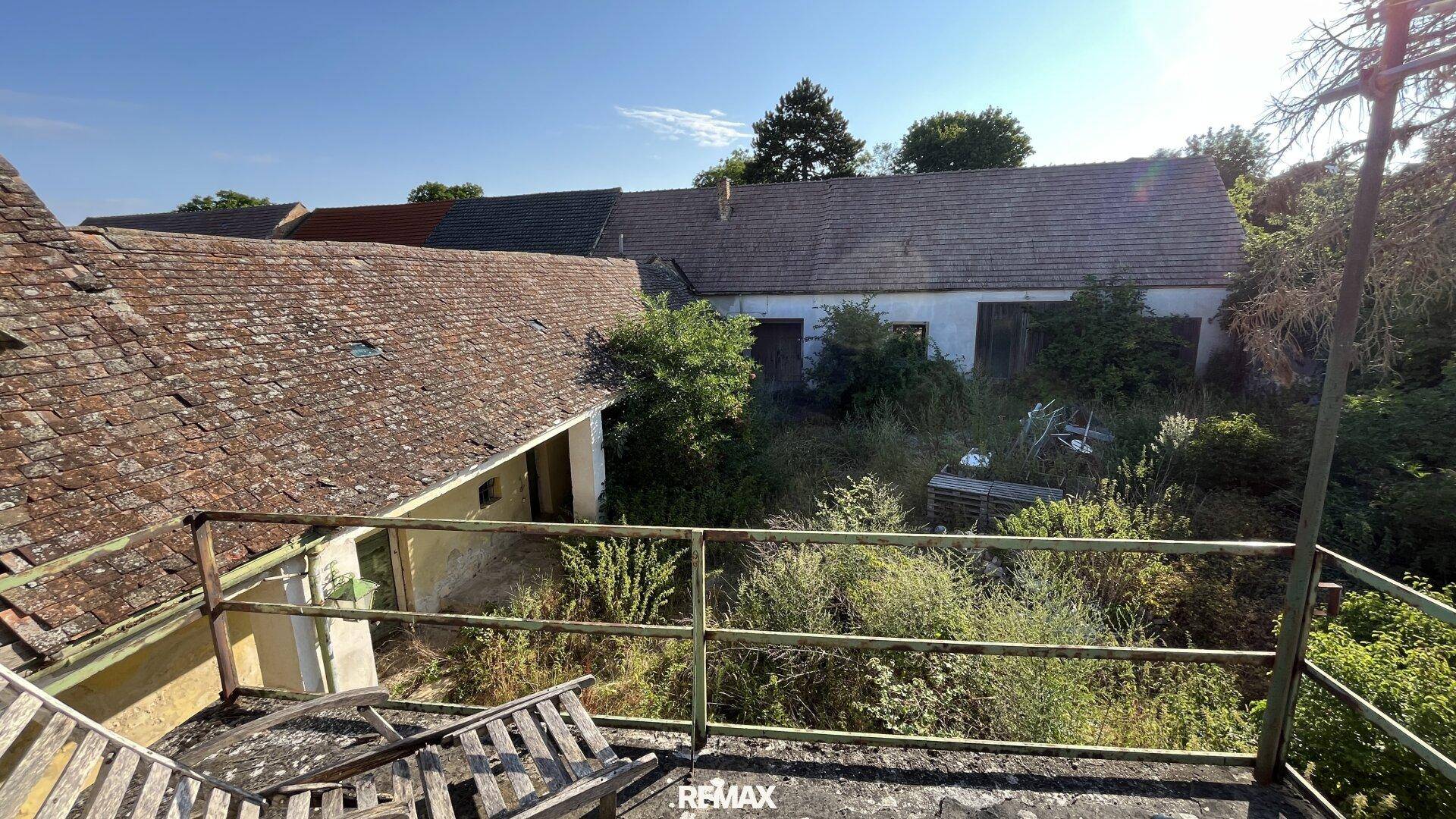 Überblick über mehrere alte Gebäude und einen verwilderten Gartenbereich unter klarem Himmel.