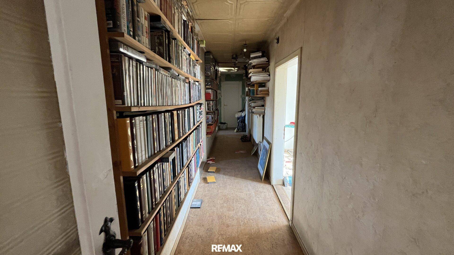Langer Flur mit Bücherregalen entlang der Wand und Teppichboden, der zu weiteren Räumen führt.