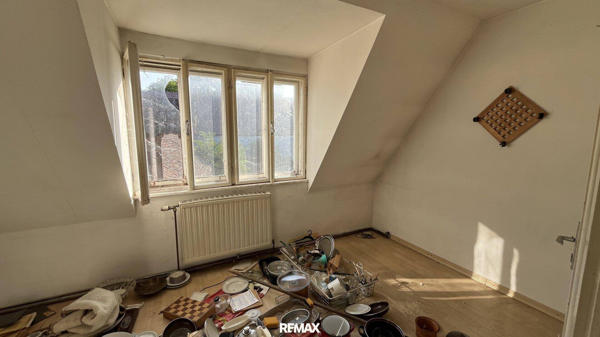 Dachzimmer mit schrägen Wänden, Laminatboden und einem Fenster, das viel Tageslicht bietet.