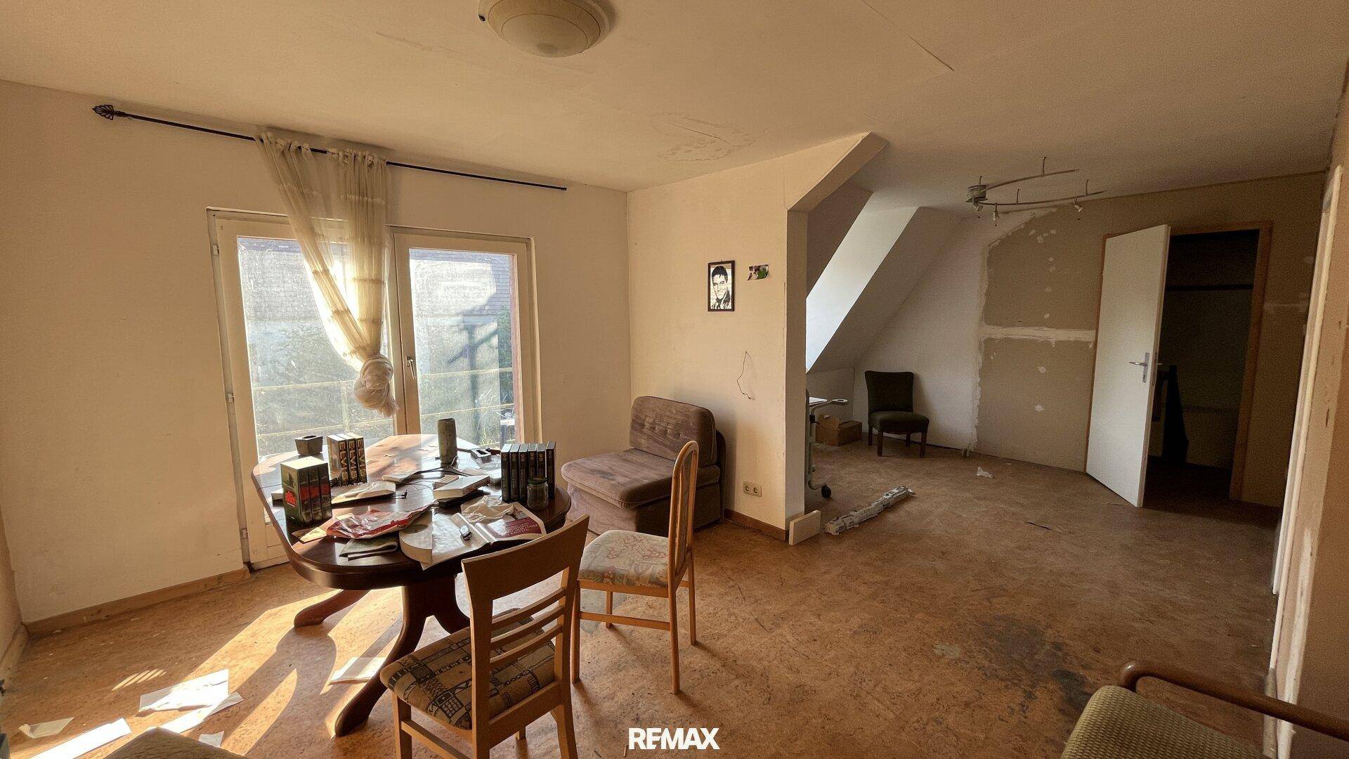 Heller Wohnbereich mit Esstisch, Stühlen und einem Fenster mit Zugang nach draußen.