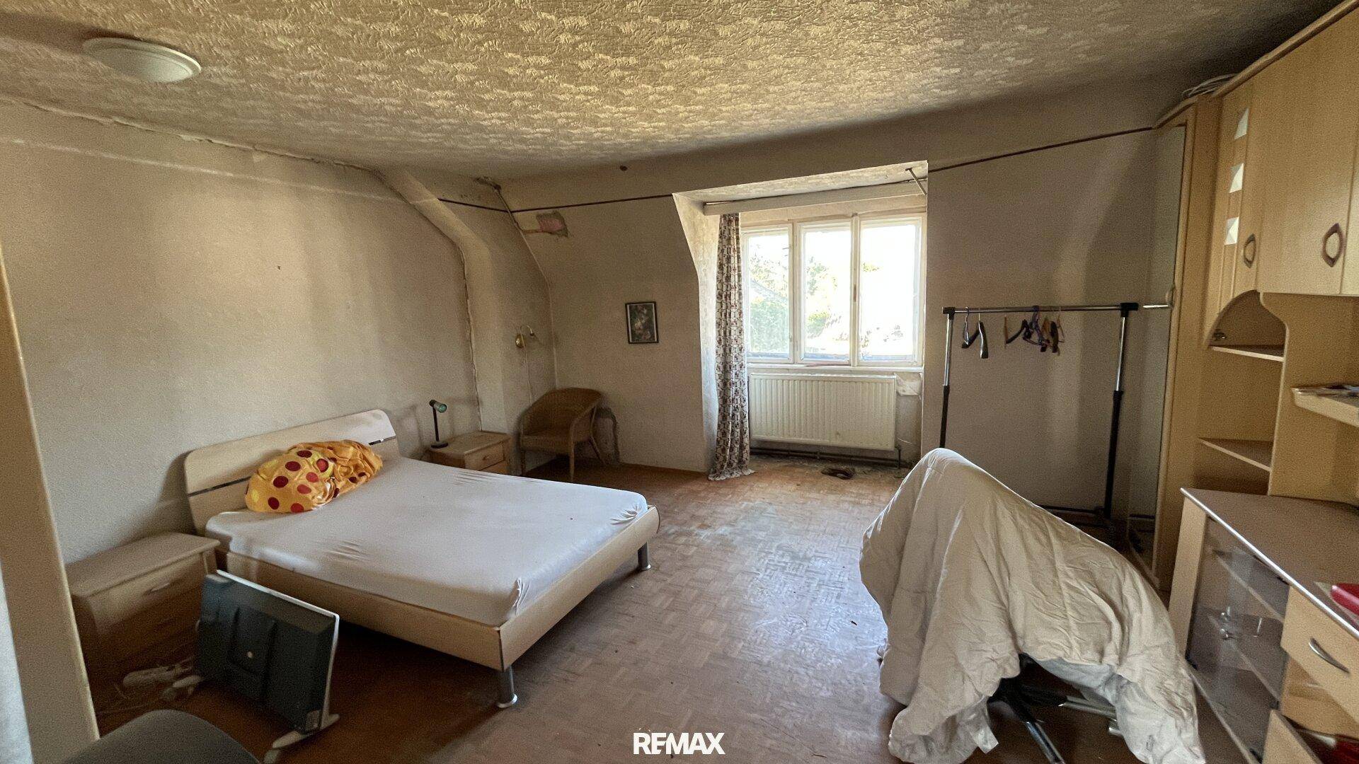 Geräumiges Schlafzimmer mit Holzboden, Bett und Kleiderschrank, beleuchtet durch ein großes Fenster.