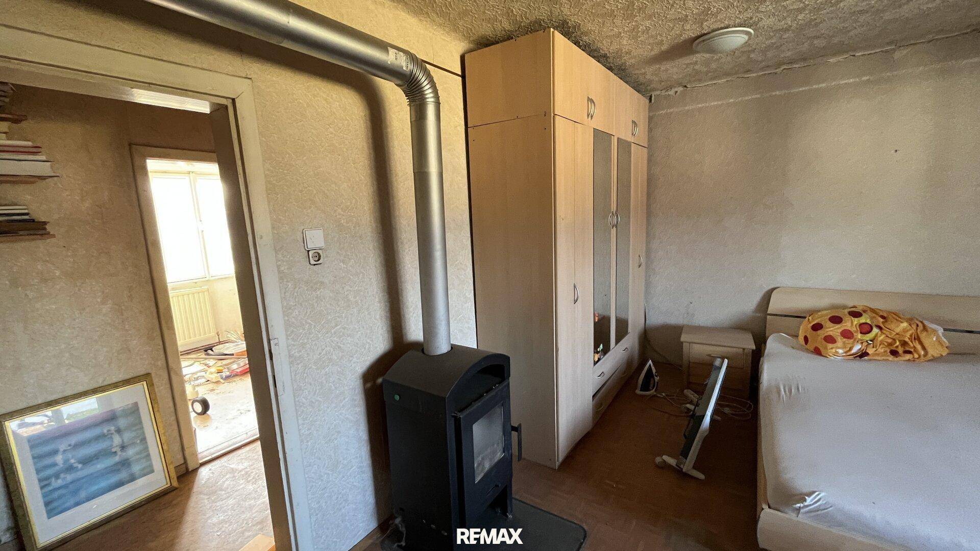 Schlafzimmer mit Holzofen, Kleiderschrank und Bett, das eine gemütliche Atmosphäre schafft.