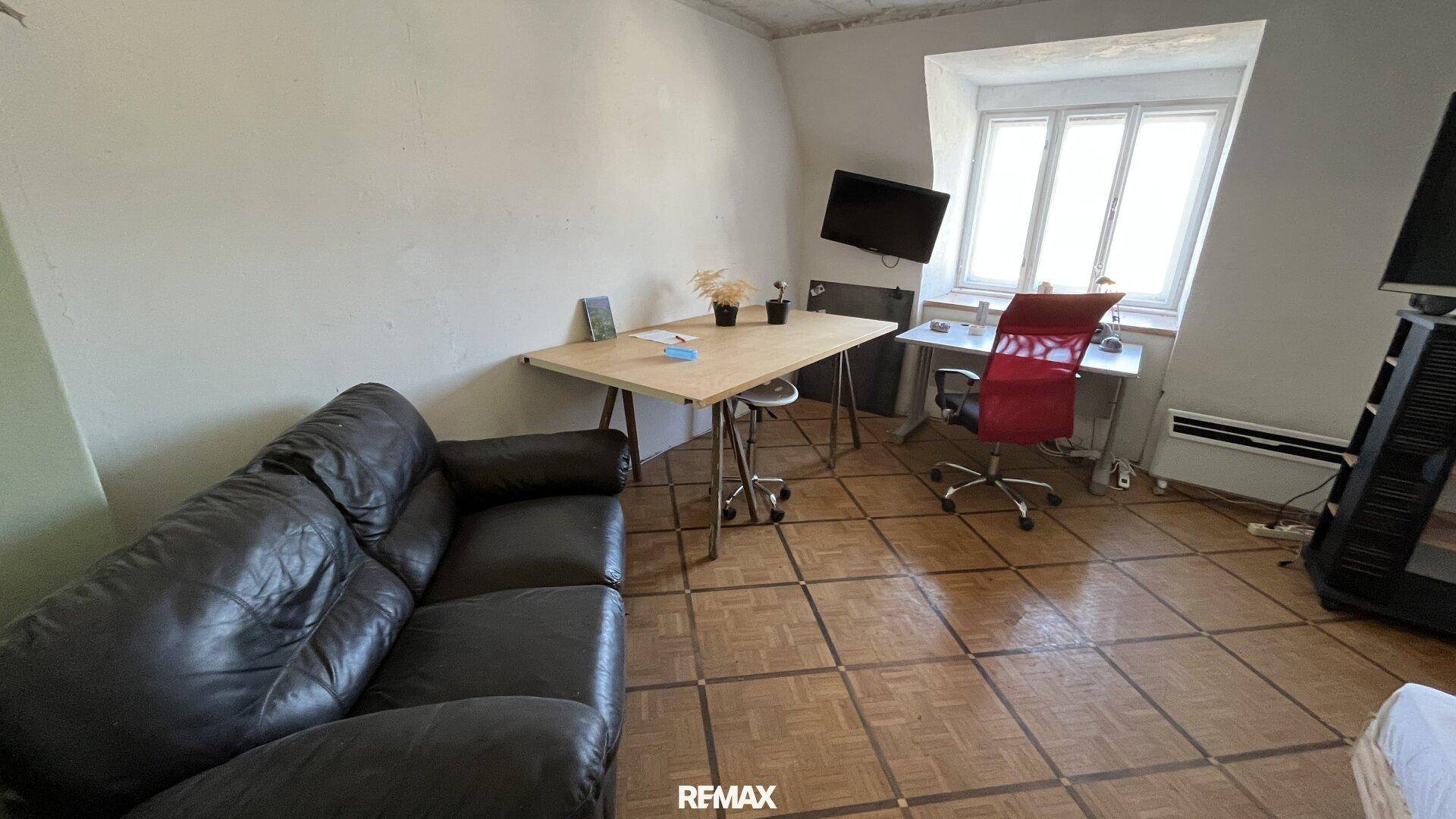 Wohnzimmer mit Ledersofa, Schreibtisch und Holzboden, hell durch das Fenster.