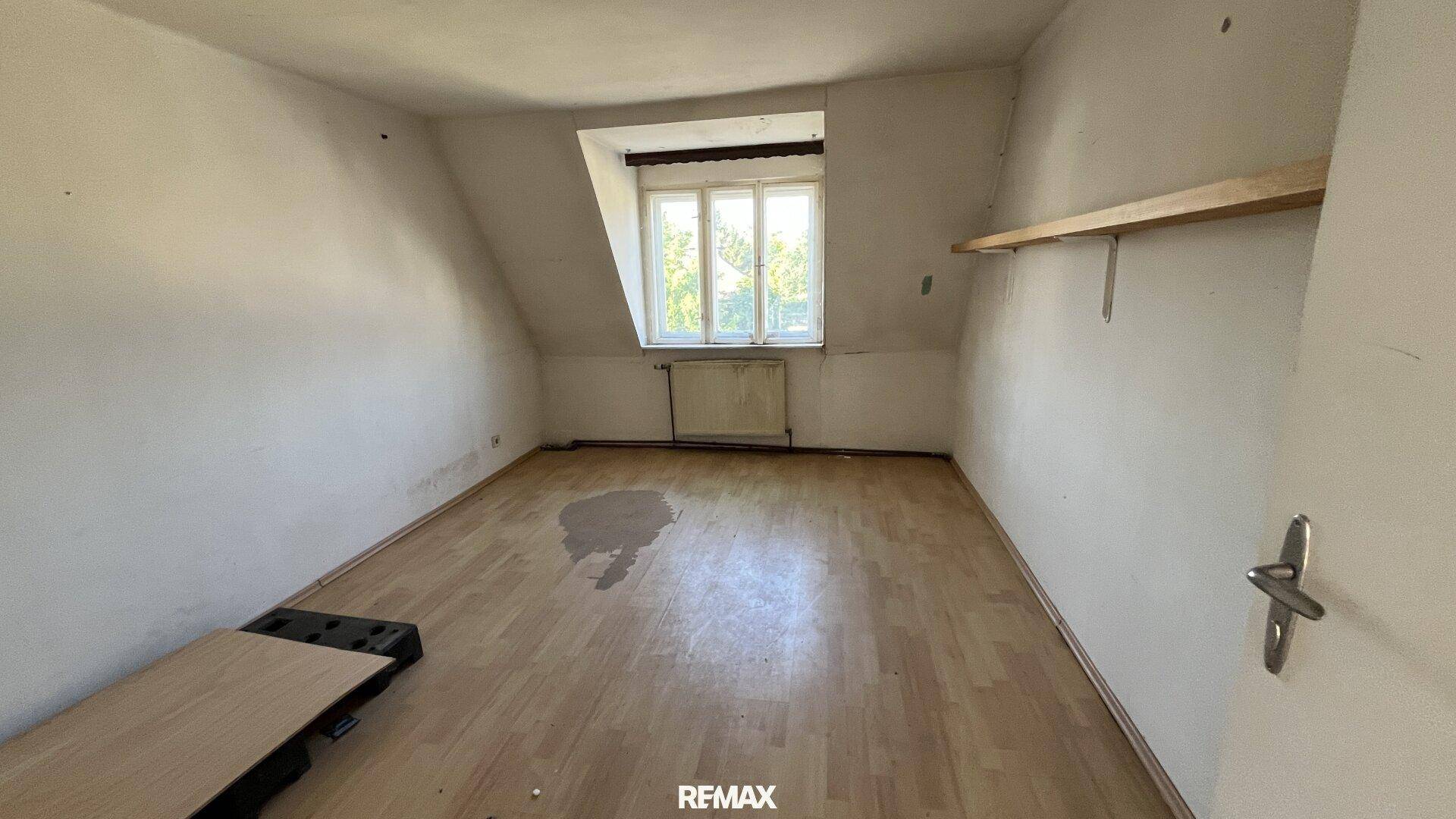 Dachzimmer mit schrägen Wänden, Laminatboden und einem Fenster mit Blick ins Grüne.