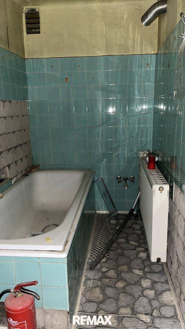 Altes Badezimmer mit türkisfarbenen Fliesen, Badewanne und einem Heizkörper, renovierungsbedürftig.