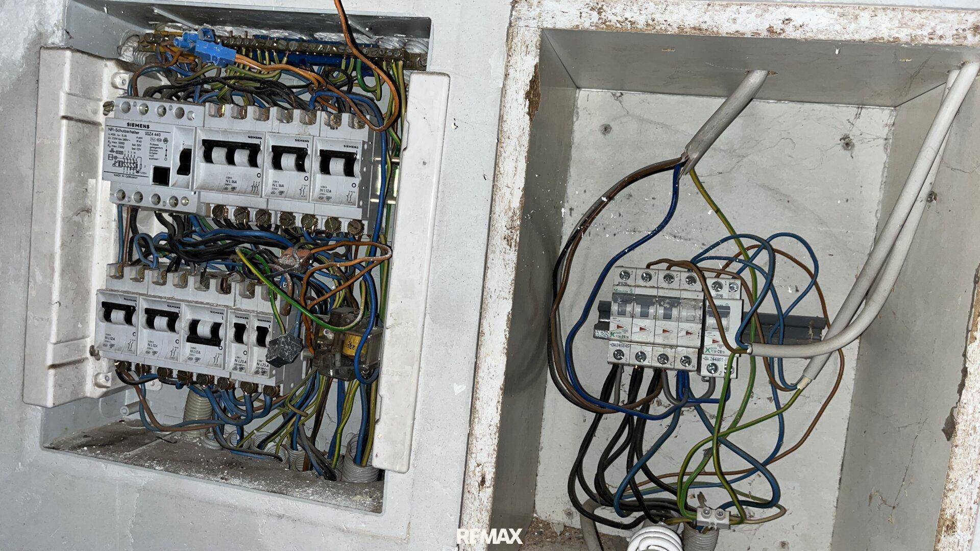 Offene elektrische Schaltkästen mit vielen Kabeln, die auf eine Renovierung hindeuten.