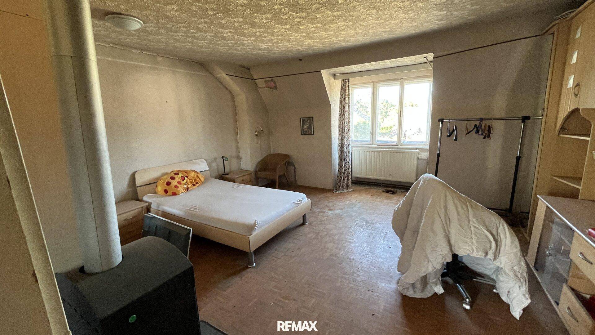 Geräumiges Schlafzimmer mit Holzboden, Bett, Kleiderschrank und einem Holzofen für Wärme.