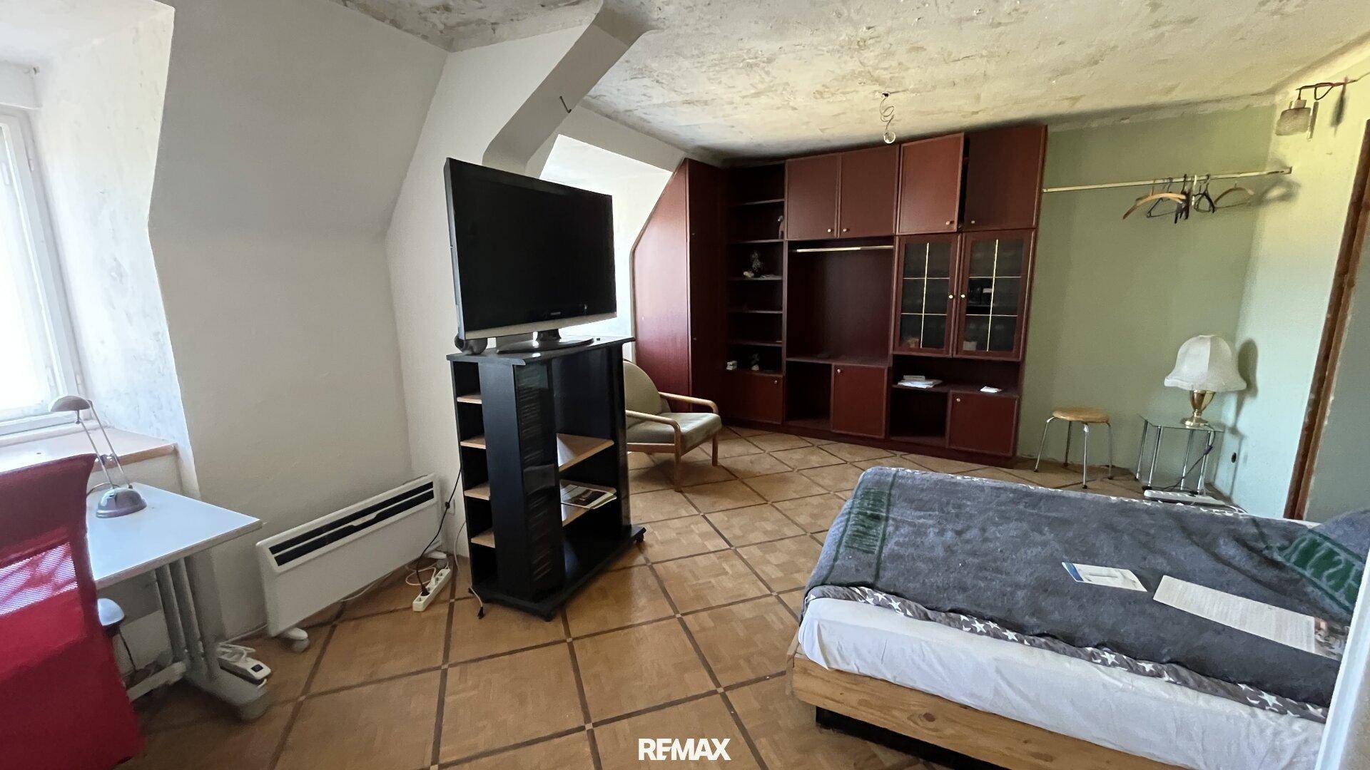 Schlafzimmer im Dachgeschoss mit schrägen Wänden, Fliesenboden und einem großen Kleiderschrank.