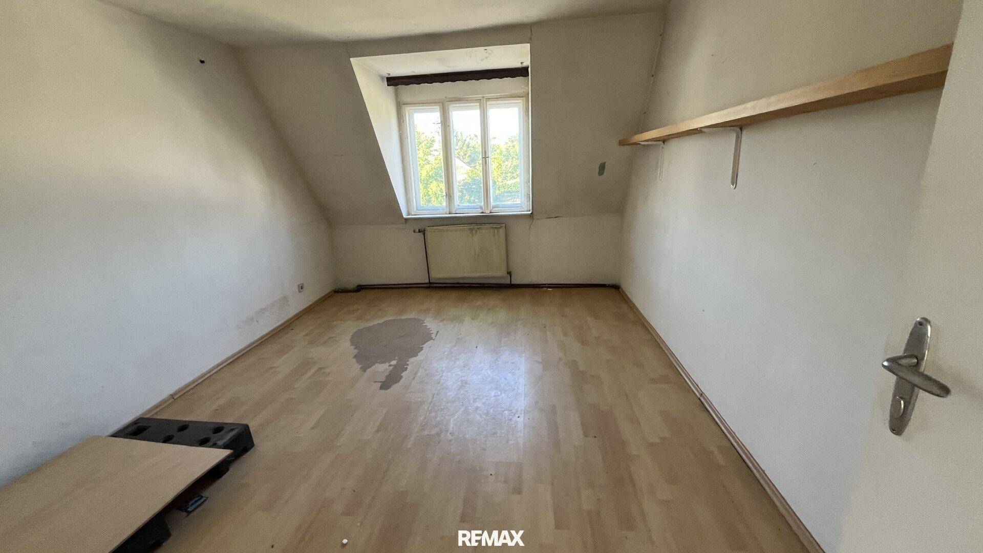 Dachzimmer mit schrägen Wänden, Laminatboden und einem Fenster mit Blick ins Grüne.