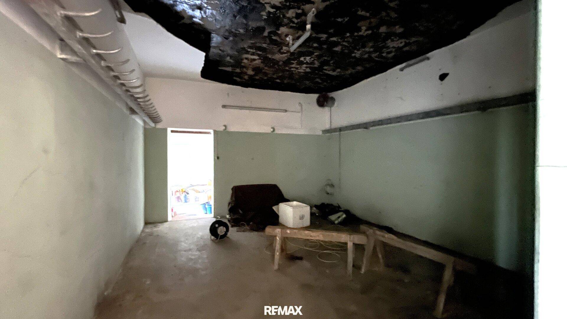 Rohbau-Innenraum mit Betonboden, zweifarbigen Wänden und sichtbaren Rohren, benötigt Renovierung.
