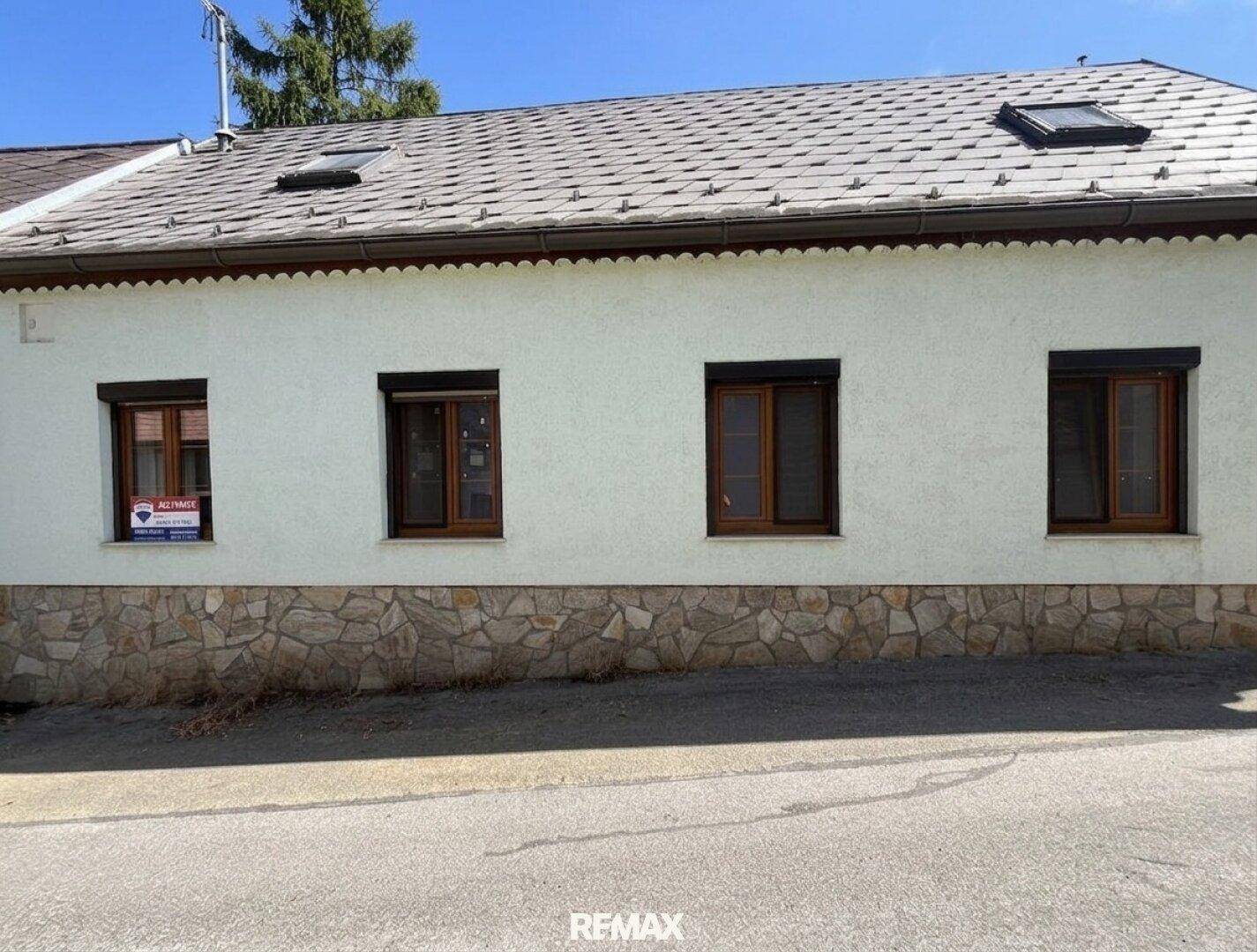 Fassade eines traditionellen Hauses mit kleinen Fenstern und einem Steinsockel.
